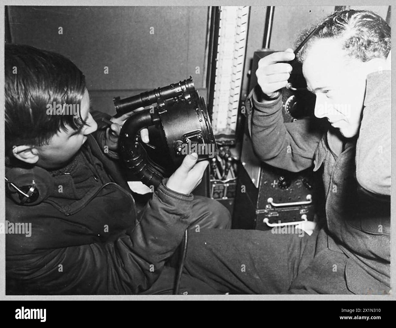 An Bord eines Liberators auf Patrouille gegen U-Boote verwendet der Funkbetreiber eine Aldis-Lampe, während der Flugingenieur seine Haare während des Betriebs aufräumt. Stockfoto