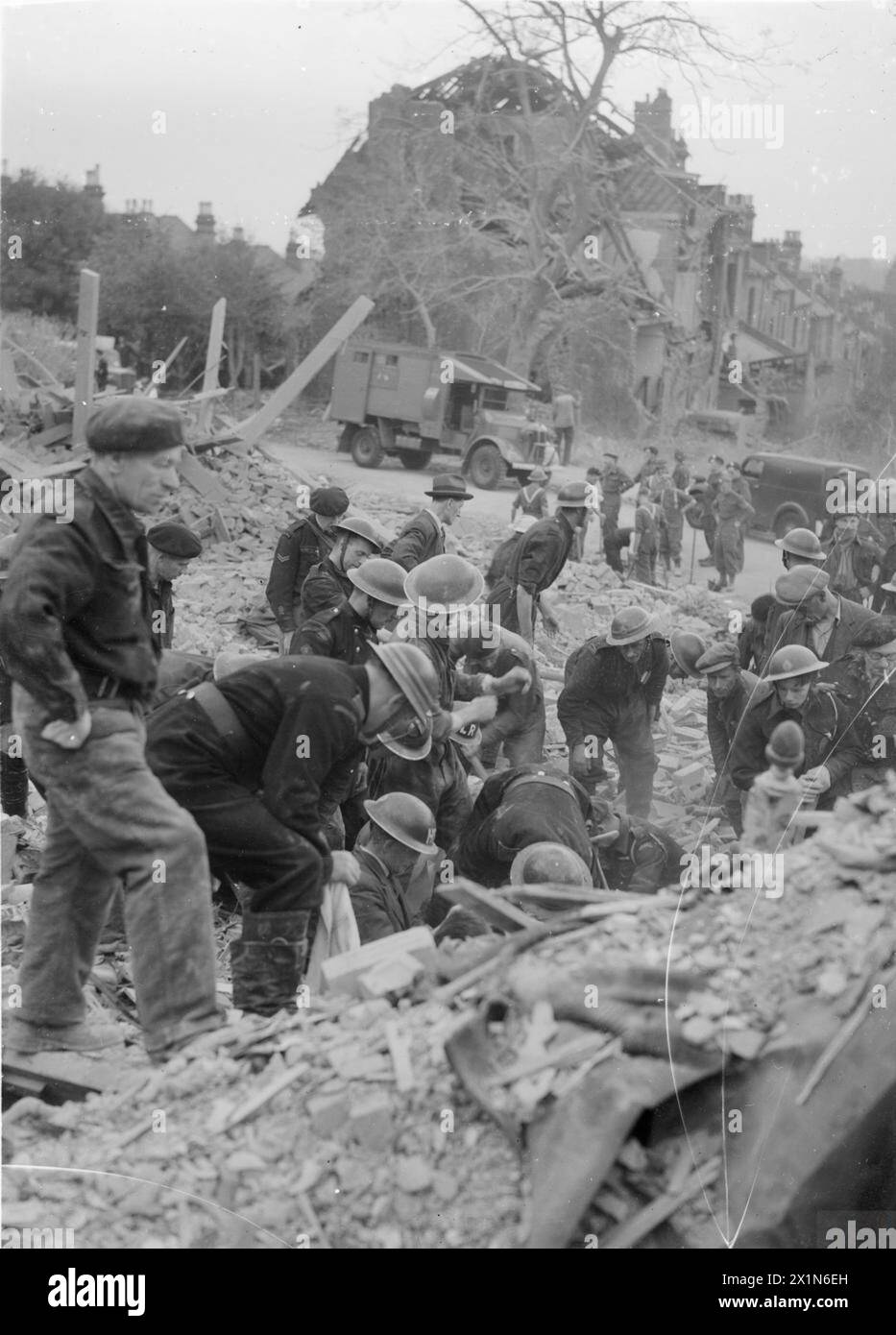 FLYING BOMB: V1 BOMBE DAMAGE IN LONDON, ENGLAND, UK, 1944 - Rettungskräfte der Zivilverteidigung suchen in einer Höhle unter einem riesigen Schutt- und Holzhaufen nach Überlebenden nach einem V1-Angriff in der Highland Road und Lunham Road in Upper Norwood. Im Hintergrund kann man eine Gruppe von Männern des Pioneer Corps sehen, die auf Anweisungen warten, wo man graben sollte. Ein Krankenwagen der amerikanischen Ambulanz Großbritannien kann auch direkt vor einem Haus gesehen werden, das ebenfalls durch die Bombe schwer beschädigt wurde, British Army, Royal Pioneer Corps Stockfoto