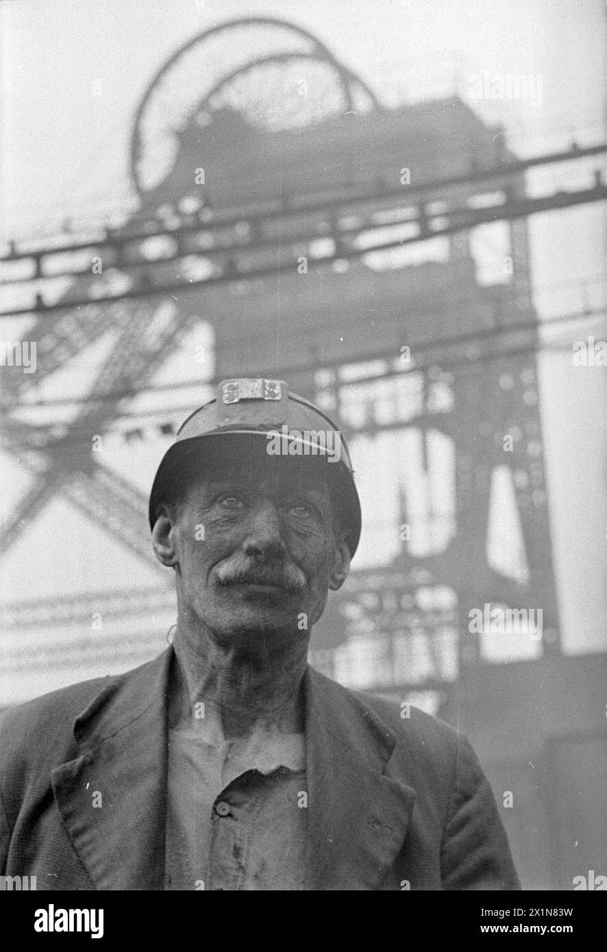 MAN OF THE MINE: LIFE AT THE COAL FACE, GROSSBRITANNIEN, 1942 - Ein auffälliges Kopf-und-Schultern-Porträt des Bergarbeiters Fred Woolhouse. Im Hintergrund sieht man die Grubenkopfmaschine, die über ihm thront. Stockfoto