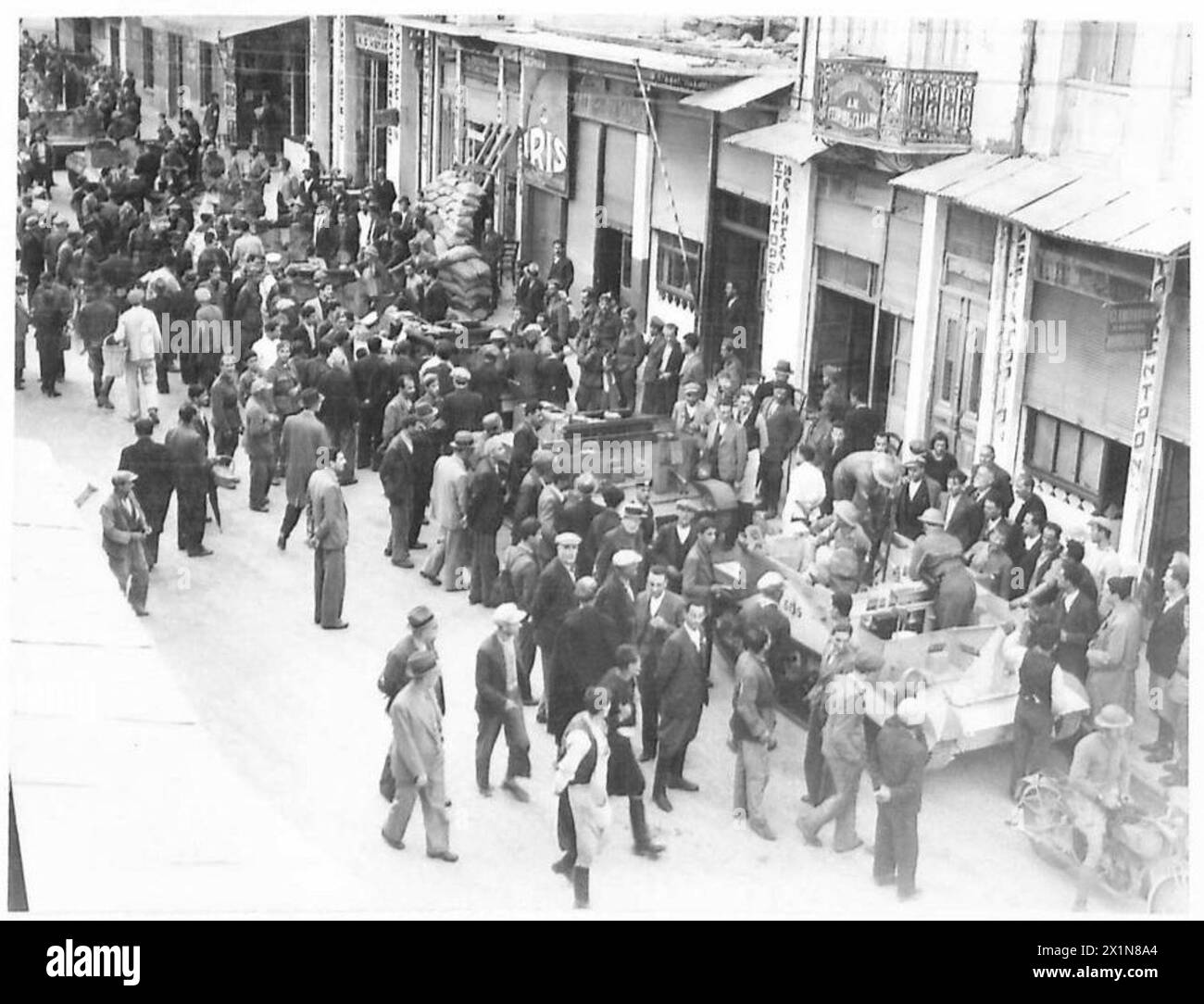 Eine mechanisierte Kolonne der britischen Armee ist von Menschenmassen umgeben, während sie durch eine Stadt in Griechenland fährt. Stockfoto