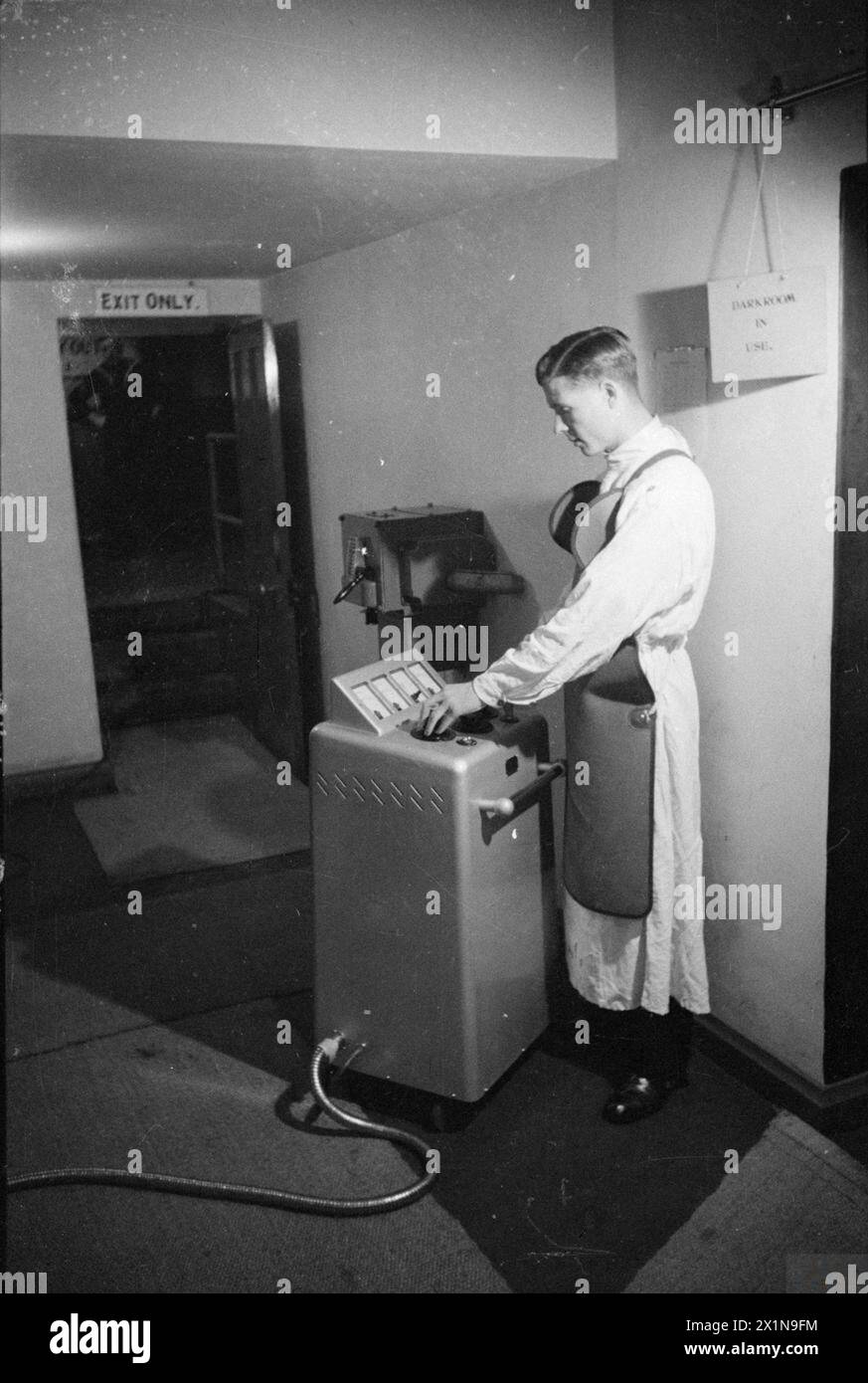 Im Jahr 1940 unterziehen sich Neueinsteiger in der Royal Navy Barracks in Chatham Röntgenuntersuchungen des Pulmographen. Jeder Mann trägt eine nummerierte Karte, die Gewicht, Größe und Alter aufzeichnet, während ein Bediener am Kontrolltisch eine Bleischürze trägt. Stockfoto