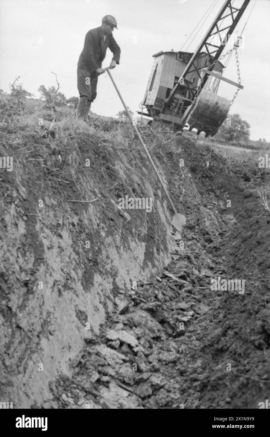 Ein Landarbeiter in Huntingdonshire, England, 1942 begrenzen einen neuen Deich auf aufbereitetem Land, während ein Schleppbagger in Betrieb ist und Gräben gräbt, um die Entwässerung von schwerem Lehmboden für den Anbau zu verbessern. Stockfoto