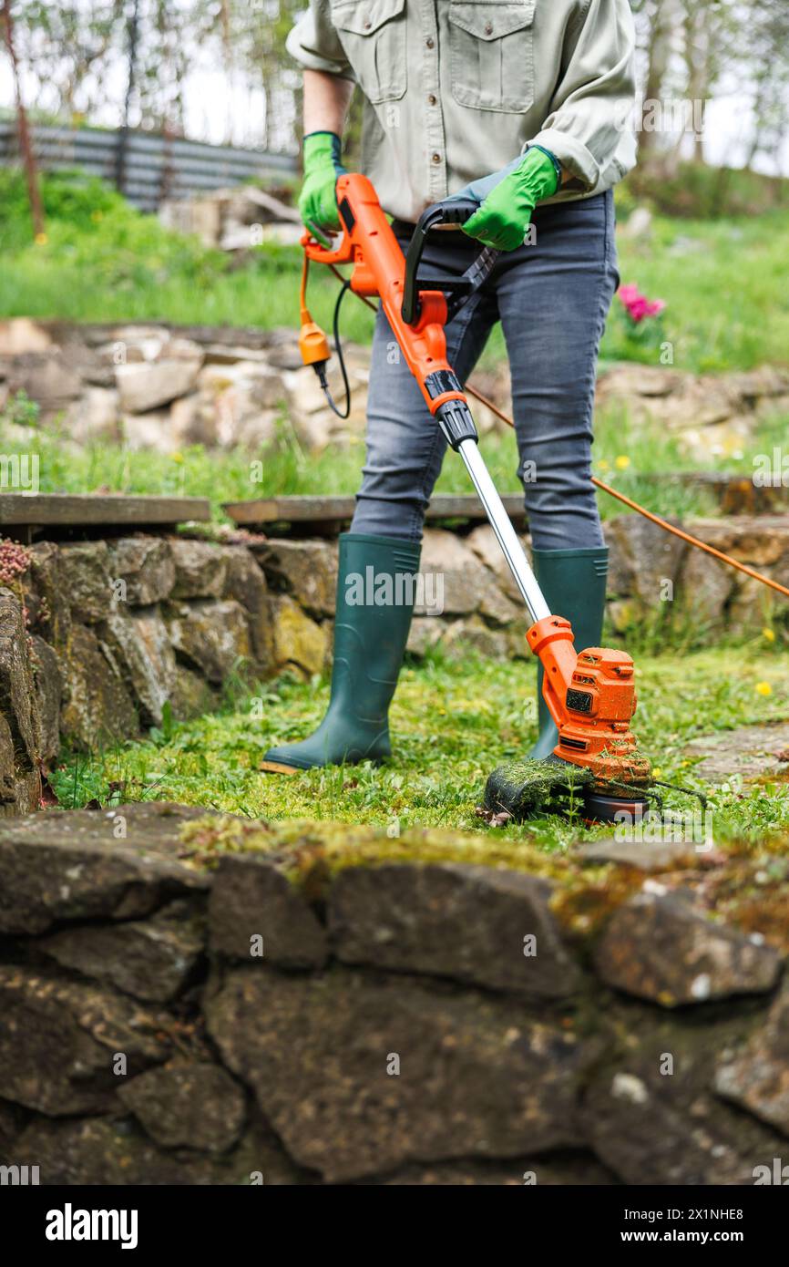Fadentrimmer. Frau schneidet Gras in der nächsten Steinmauer im Garten. Rasenpflege Stockfoto