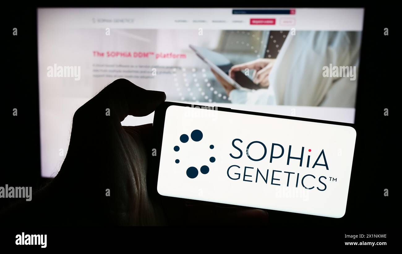 Person mit Smartphone mit Logo des Schweizer Gesundheitssoftware-Unternehmens Sophia Genetics SA vor der Website. Schwerpunkt auf dem Display des Telefons. Stockfoto
