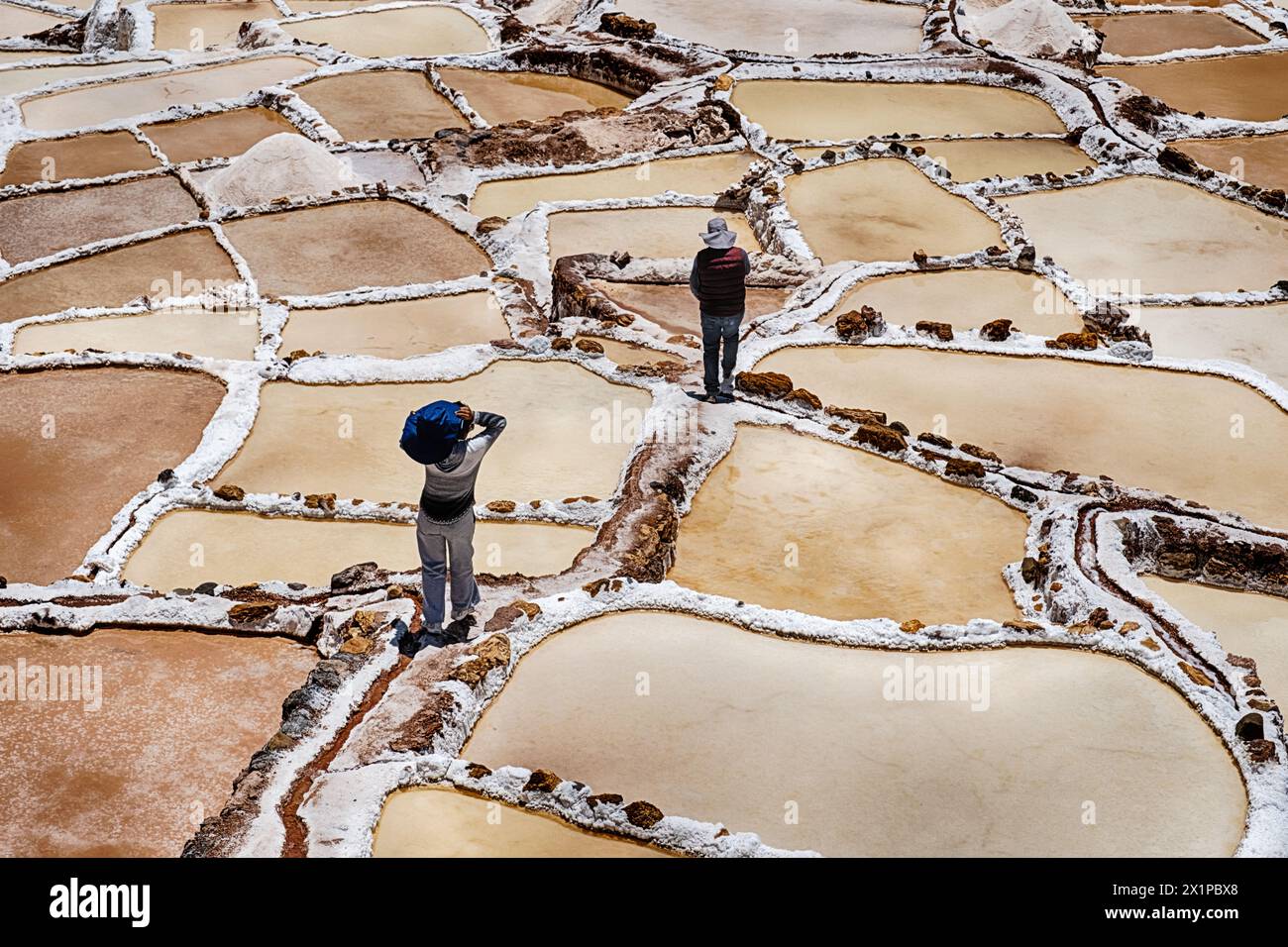 SALINERAS DE MARAS, PERU - 2. OKTOBER 2023: Zwei anonyme Arbeiter gehen durch Wanderwege zwischen den Salineras de Maras in Peru Stockfoto