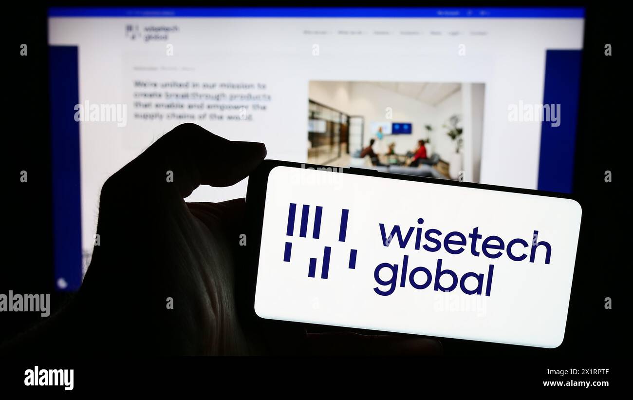 Person mit Smartphone und Logo des australischen Softwareunternehmens WiseTech Global Limited vor der Website. Schwerpunkt auf dem Display des Telefons. Stockfoto