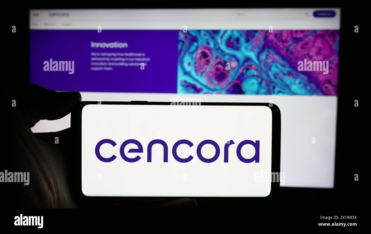 Person, die ein Mobiltelefon mit dem Logo des US-Arzneimittelgroßhandelsunternehmens Cencora Inc. Vor der Website des Unternehmens hält. Schwerpunkt auf dem Display des Telefons. Stockfoto
