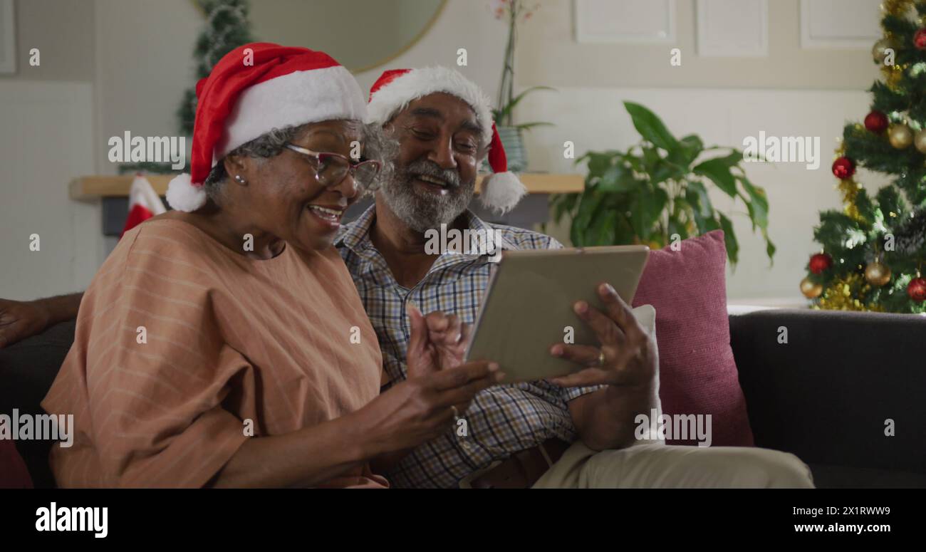 Ein hochrangiges birassisches Paar mit Weihnachtsmützen und Blick auf ein Tablet Stockfoto