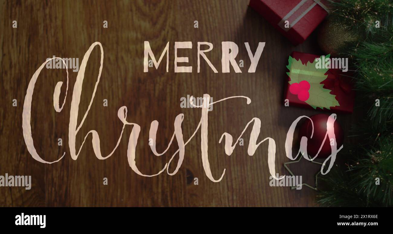 Frohe Weihnachten in Kursivschrift auf Holzoberfläche, umgeben von Weihnachtsdekor Stockfoto