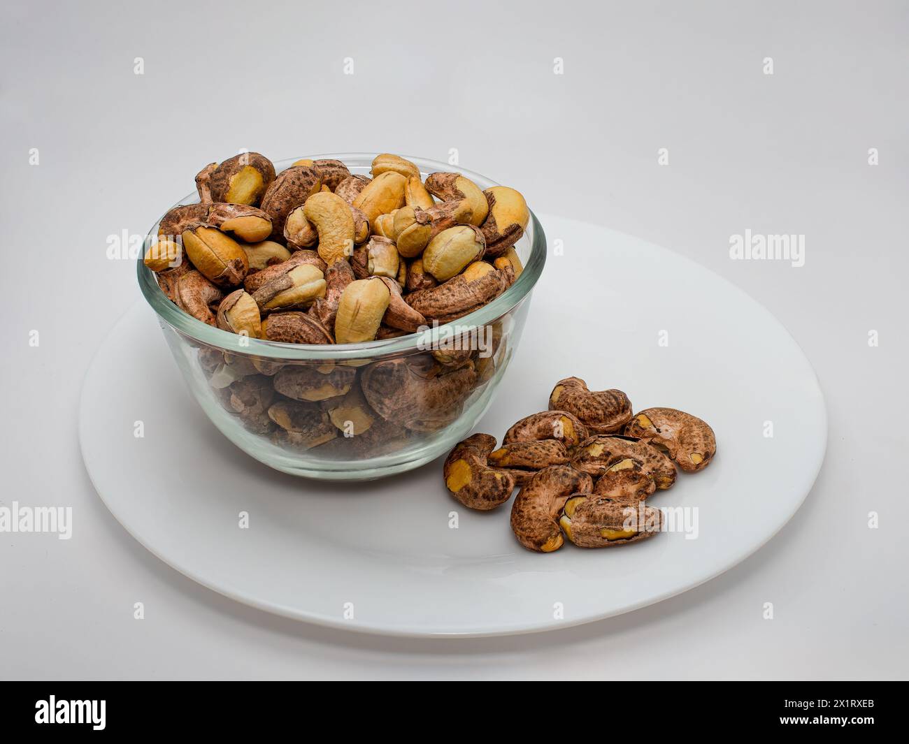 Charcole geröstete Cashewnüsse auf der Glasschale mit weißem Hintergrund, Cashewnüsse sehen sehr natürlich aus, ohne die Haut mit roh und geröstet mit zu schälen Stockfoto