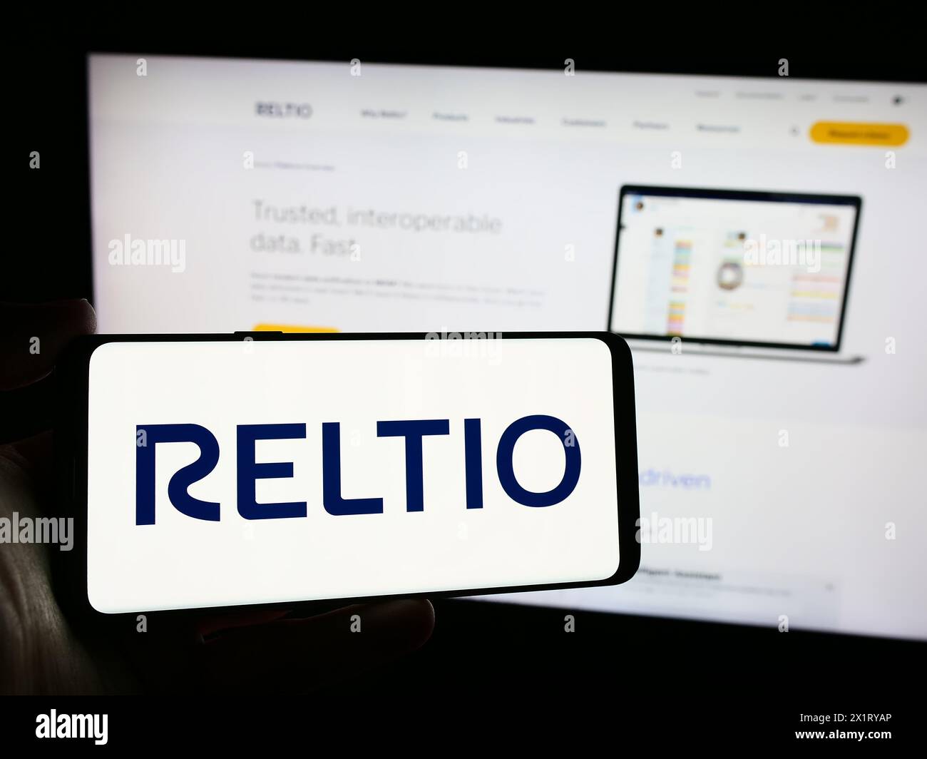 Person, die ein Mobiltelefon mit dem Logo des amerikanischen Softwareunternehmens Reltio Inc. Vor der Business-Webseite hält. Schwerpunkt auf dem Display des Telefons. Stockfoto