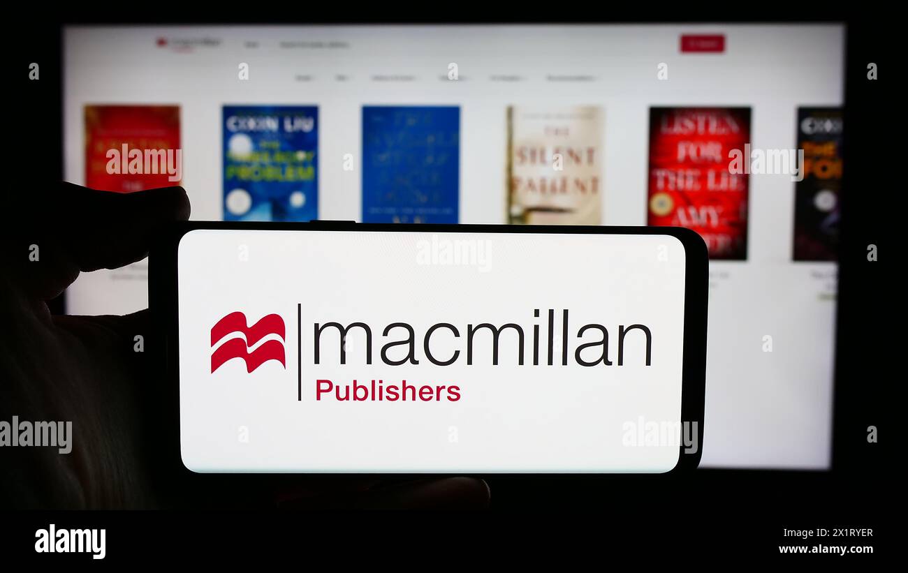 Person, die ein Handy mit dem Logo des britischen Verlags Macmillan Publishers vor der Webseite hält. Schwerpunkt auf dem Display des Telefons. Stockfoto