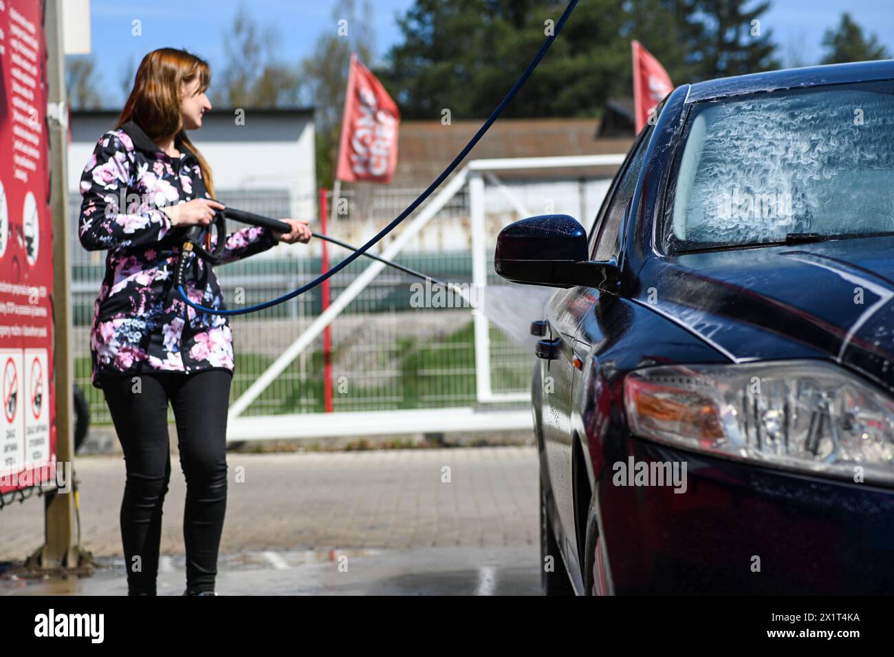 Eine Frau wäscht ein Auto in einer Autowaschanlage. Sie hält eine Wasserdruckpistole in der Hand. Stockfoto