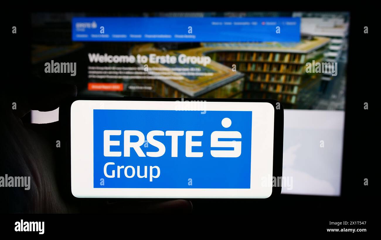 Person mit Mobiltelefon mit Logo des österreichischen Finanzdienstleistungsunternehmens erste Group Bank AG vor der Webseite. Schwerpunkt auf dem Display des Telefons. Stockfoto