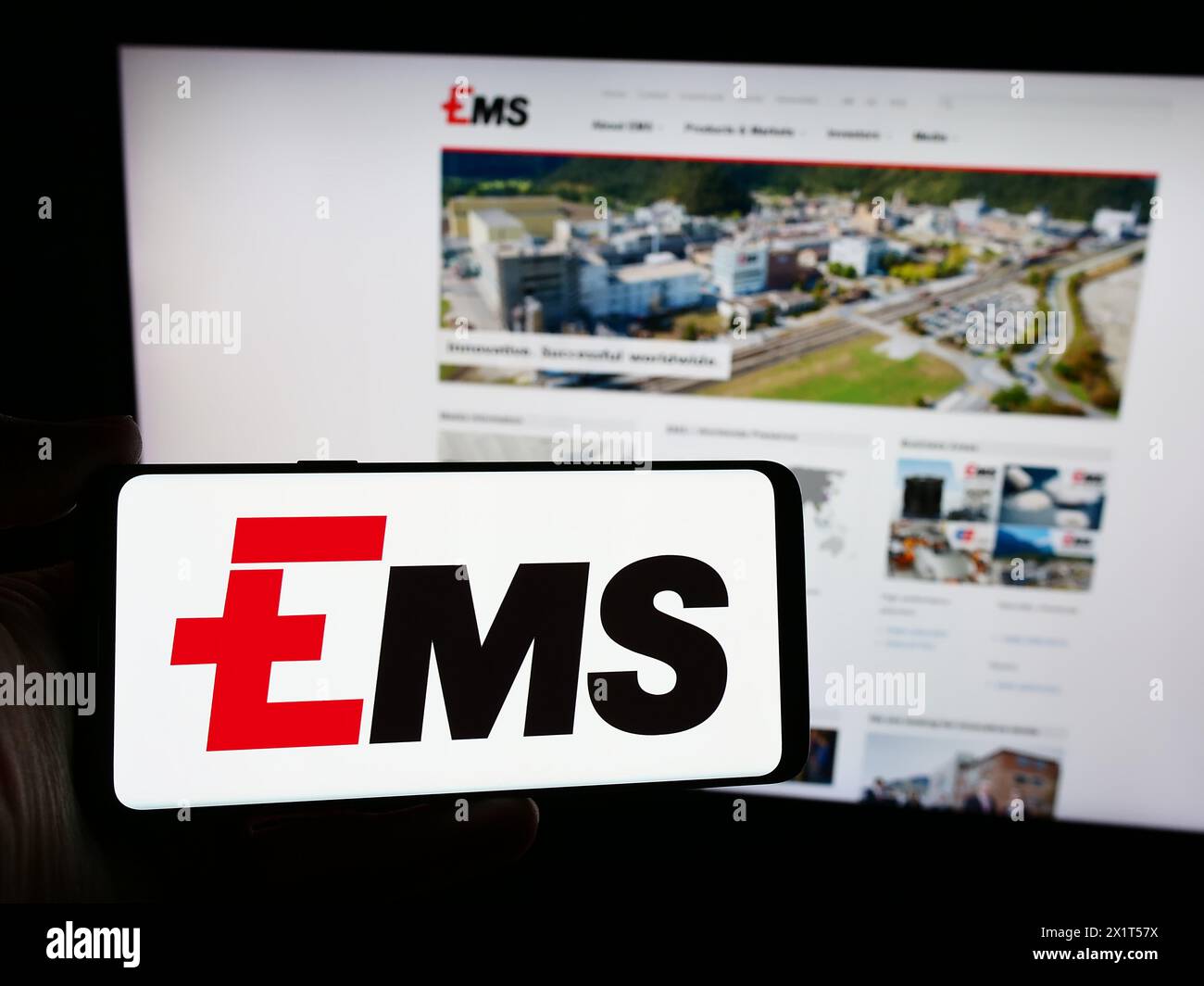 Person mit Smartphone und Logo des Schweizer Chemieunternehmens Ems-Chemie Holding AG vor der Website. Schwerpunkt auf dem Display des Telefons. Stockfoto