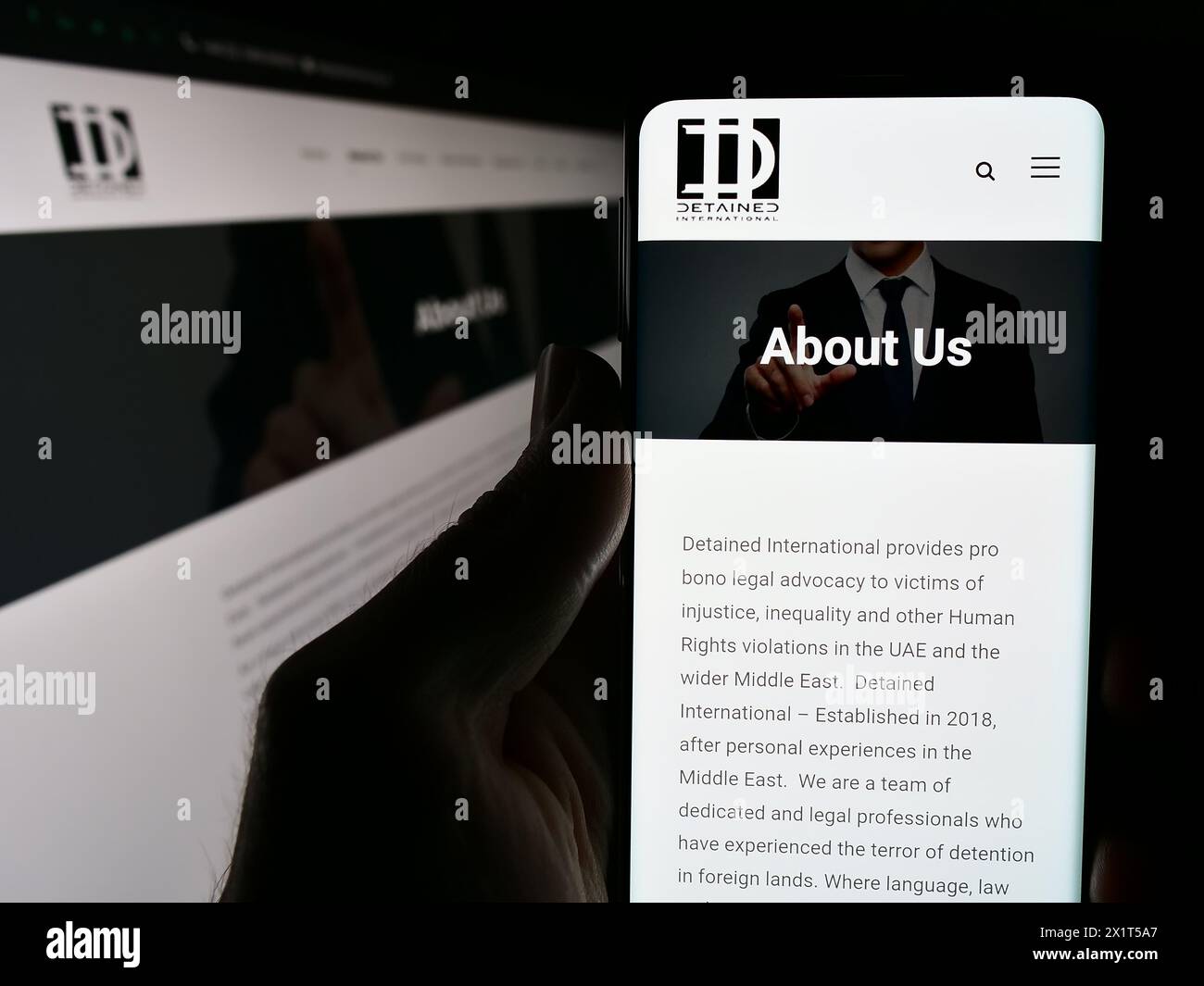 Person, die ein Handy mit Webseite und Logo der Rechtsanwaltschaft-NGO hält, hat International vor dem Monitor inhaftiert. Konzentrieren Sie sich auf die Mitte des Telefondisplays. Stockfoto
