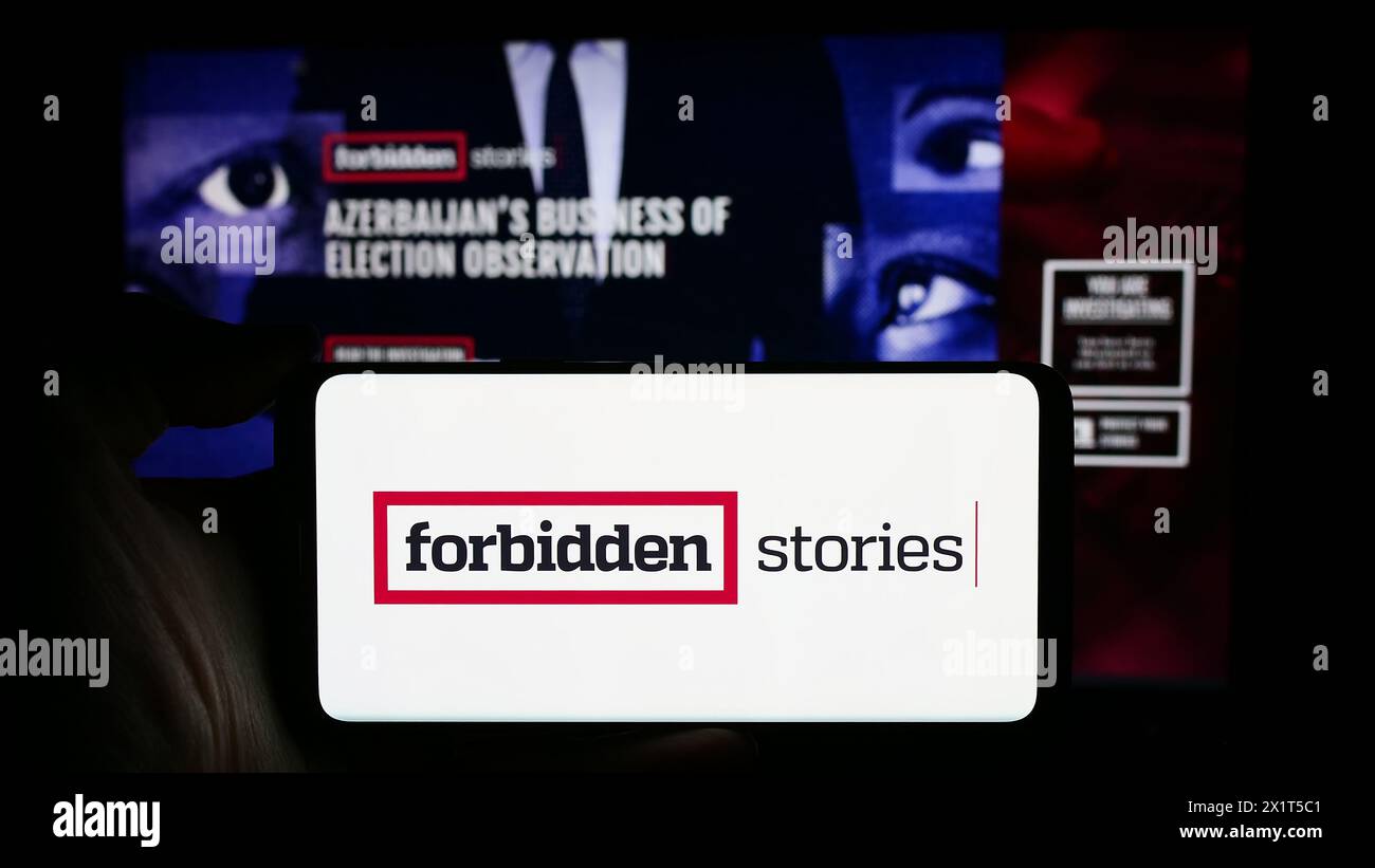 Person, die ein Handy mit dem Logo der investigativen Journalismusorganisation Forbidden Stories vor der Webseite hält. Schwerpunkt auf dem Display des Telefons. Stockfoto