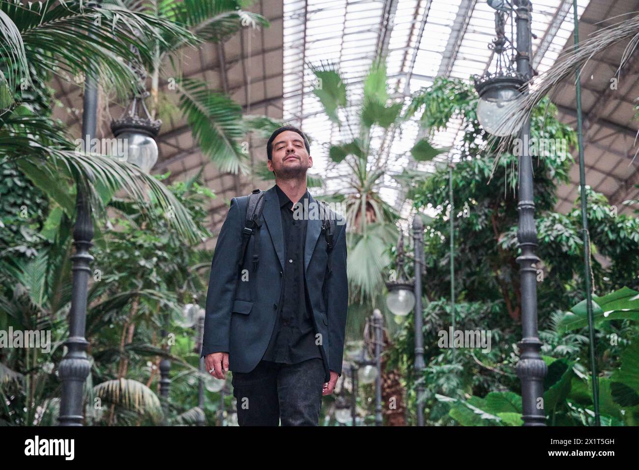 Ein junger Latino-Mann geht anmutig in ein Inneres, umgeben von üppigen grünen Pflanzen, und enthüllt die subtile Harmonie zwischen seiner persönlichen Reise und dem Stockfoto