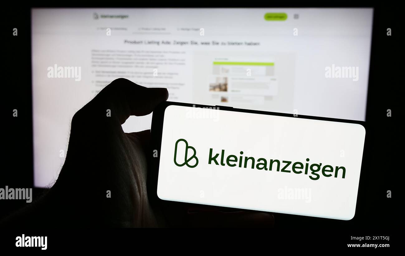 Person mit Mobiltelefon mit Logo der deutschen Kleinanzeigen-Plattformgesellschaft kleinanzeigen.de GmbH vor der Webseite. Schwerpunkt auf dem Display des Telefons. Stockfoto