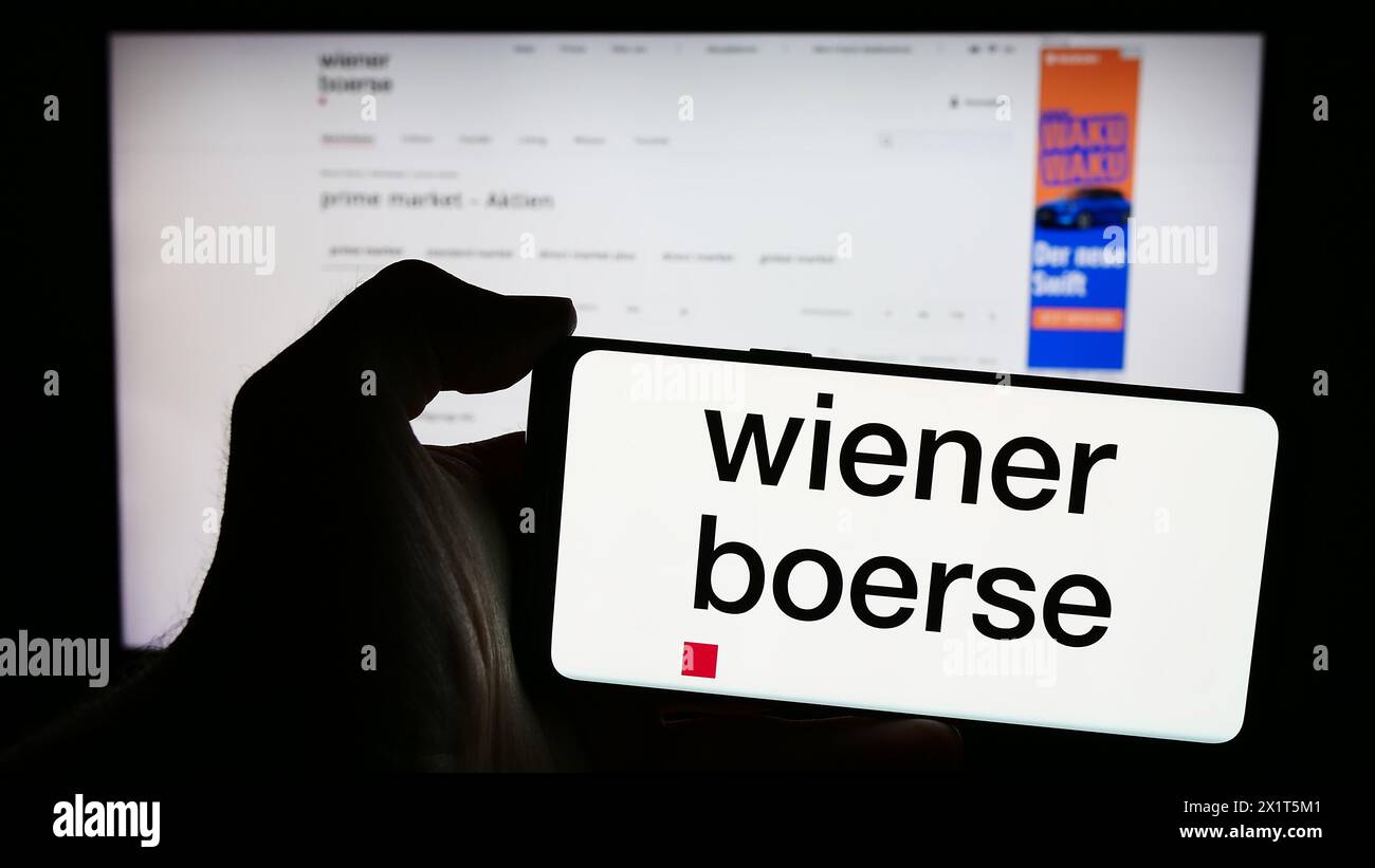 Person mit Mobiltelefon mit Logo der österreichischen Börse AG vor der Business-Webseite. Schwerpunkt auf dem Display des Telefons. Stockfoto