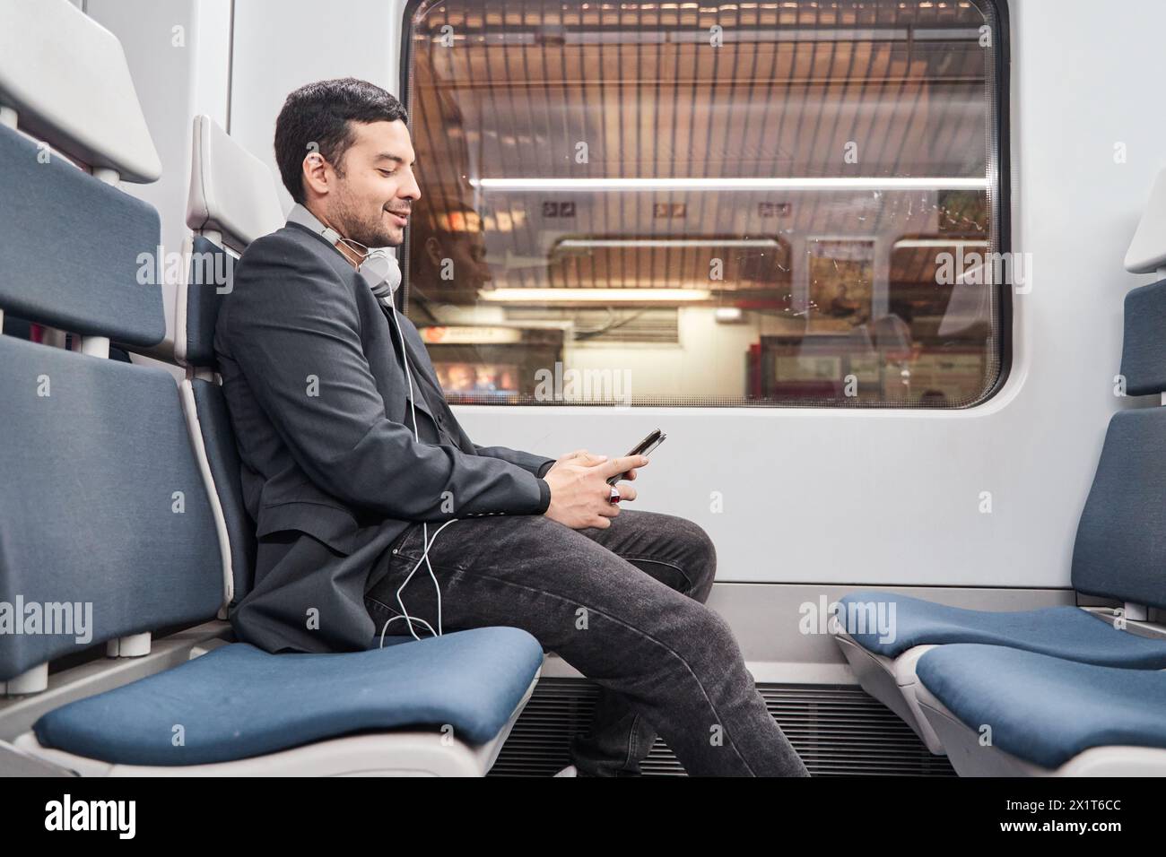 Porträt eines Mannes in einem Blazer, der im Zug sitzt und auf sein Smartphone schaut. Städtisches Verkehrskonzept Stockfoto