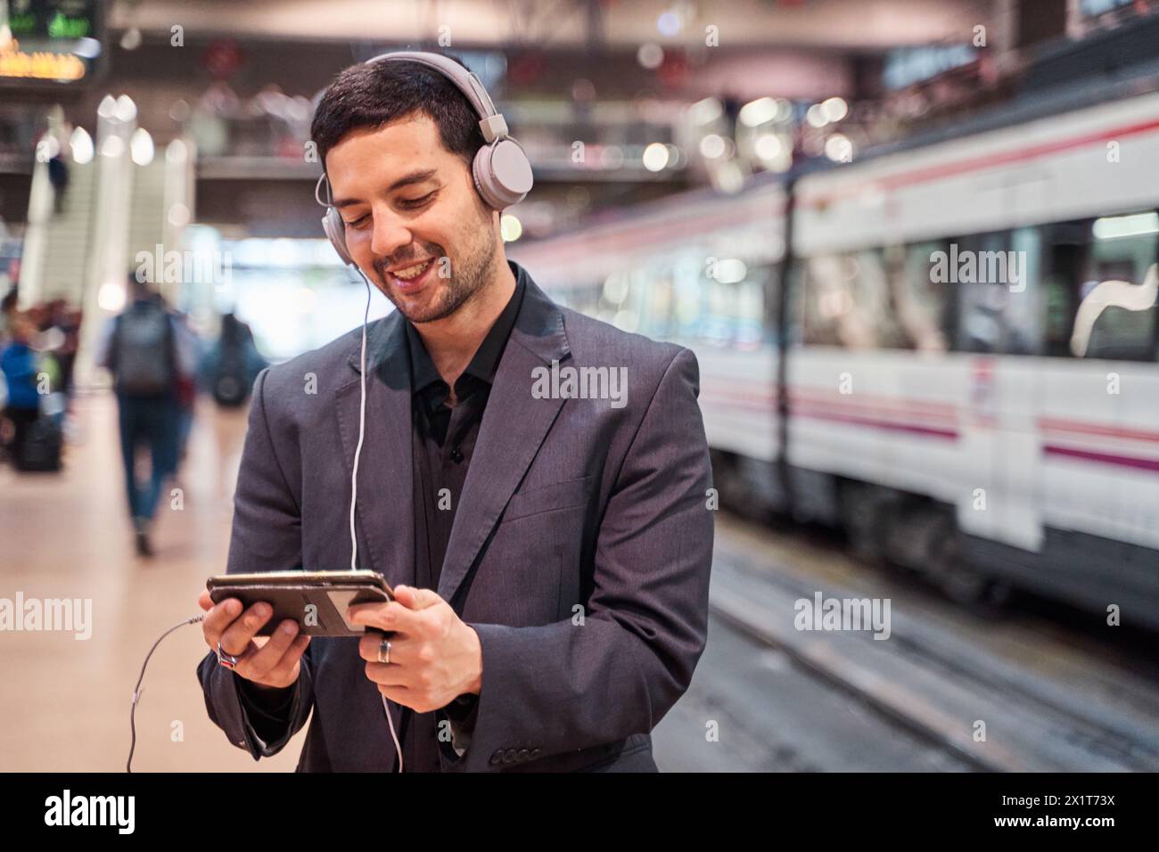Mann, der in einer unterirdischen Station mit seinem Smartphone wartet und soziale Medien ansieht oder Spiele spielt, während er sein Smartphone benutzt Stockfoto