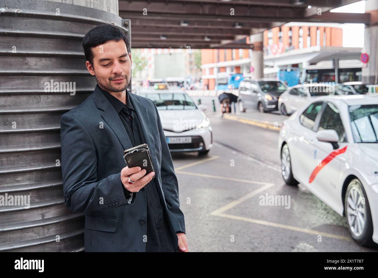 Junger lateinmann, der am Bahnhof wartet, mit seinem Smartphone in der Hand Stockfoto
