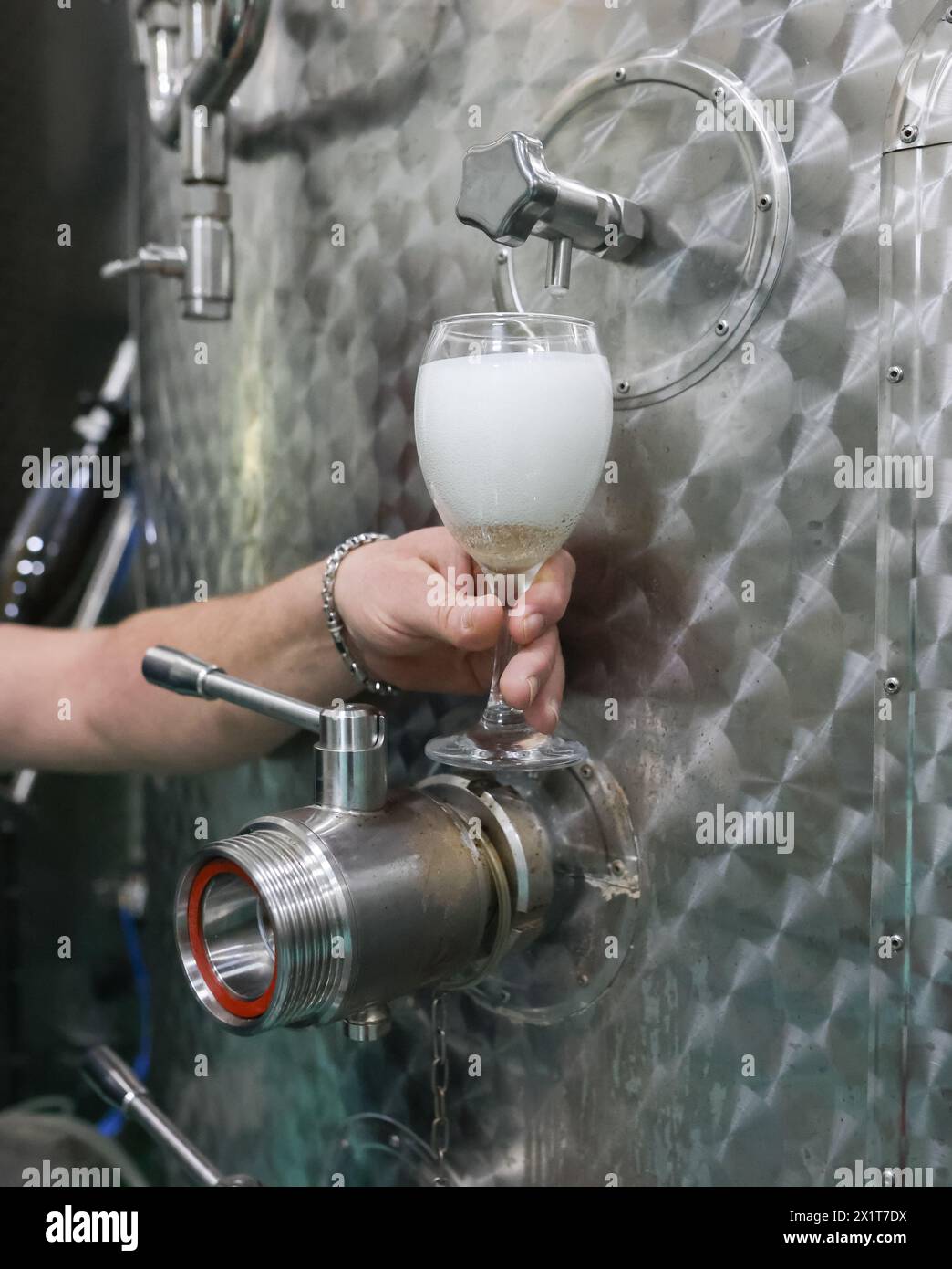 Details mit der Hand eines Winzers, der in einem modernen Weingut Sekt aus einem Metalltank in ein Glas gießt. Stockfoto