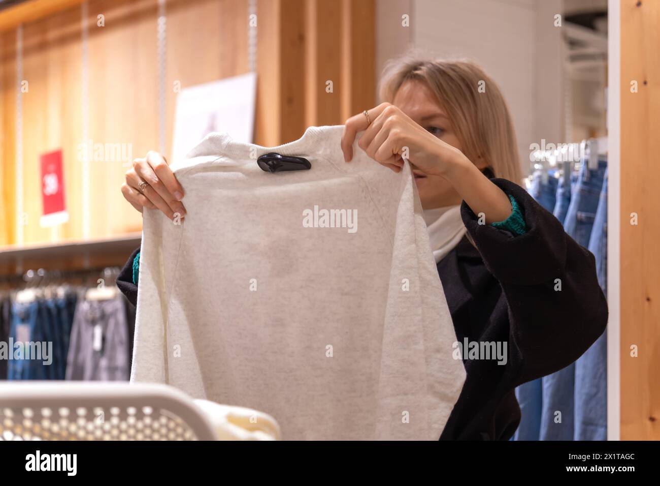 Die junge, schöne blonde Frau im Mantel sucht sich in einem Einkaufszentrum Kleidung aus Stockfoto