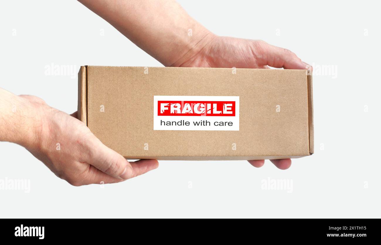 Ein rechteckiger Karton in den Händen für zerbrechliche Gegenstände, die auf einem einfachen hellen Hintergrund verpackt werden. Rotes Warnschild, Aufkleber für Verpackung „zerbrechlich“ Stockfoto