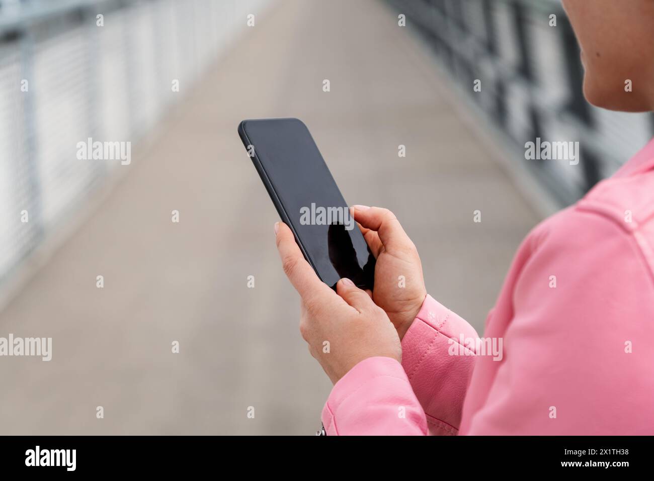 Stadträtin in rosafarbener Jacke mit schwarzem Smartphone in der Hand. Stockfoto