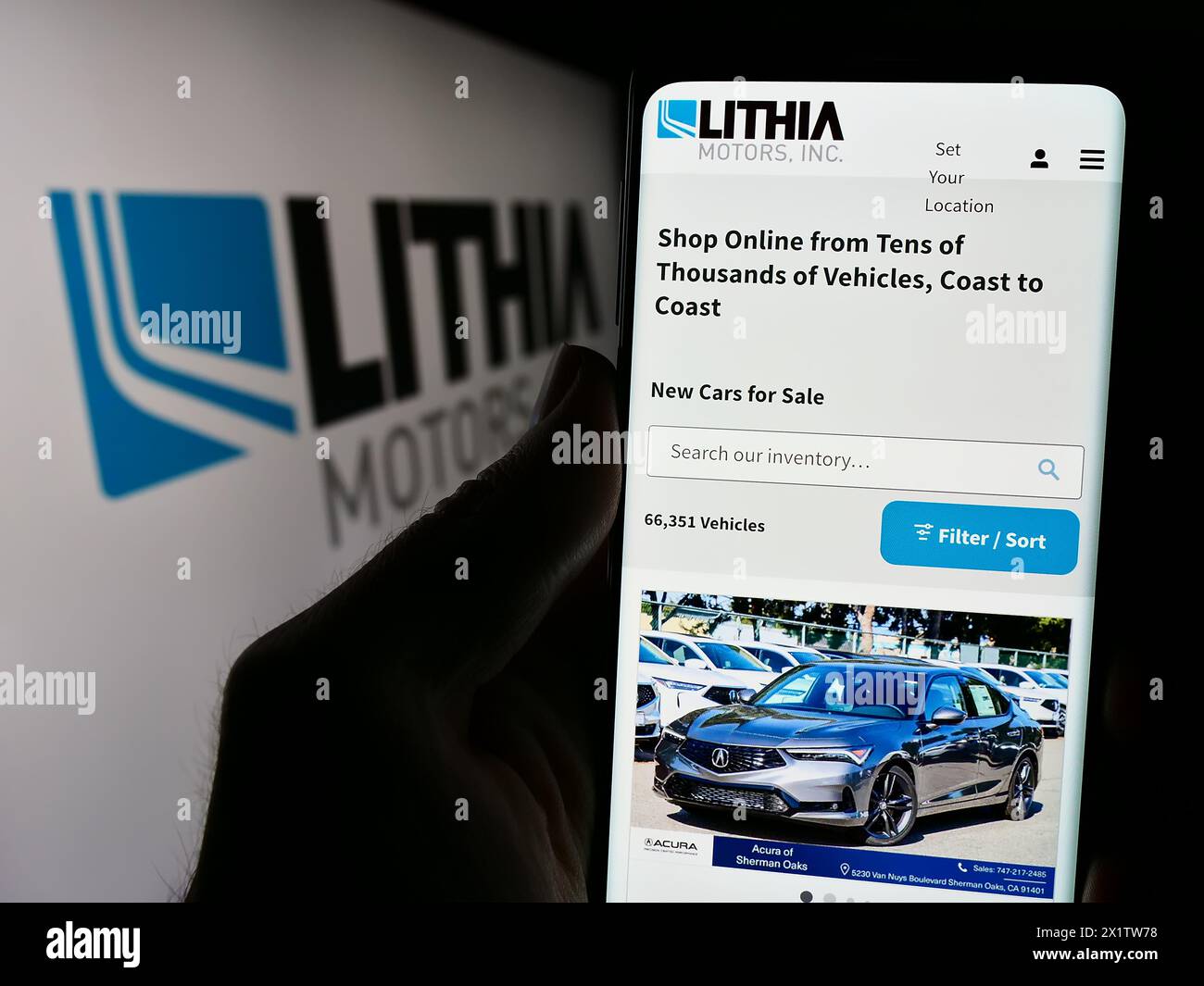 Person, die ein Mobiltelefon hält, mit der Webseite des US-amerikanischen Autohändlers Lithia Motors Inc. Vor dem Logo. Konzentrieren Sie sich auf die Mitte des Telefondisplays. Stockfoto