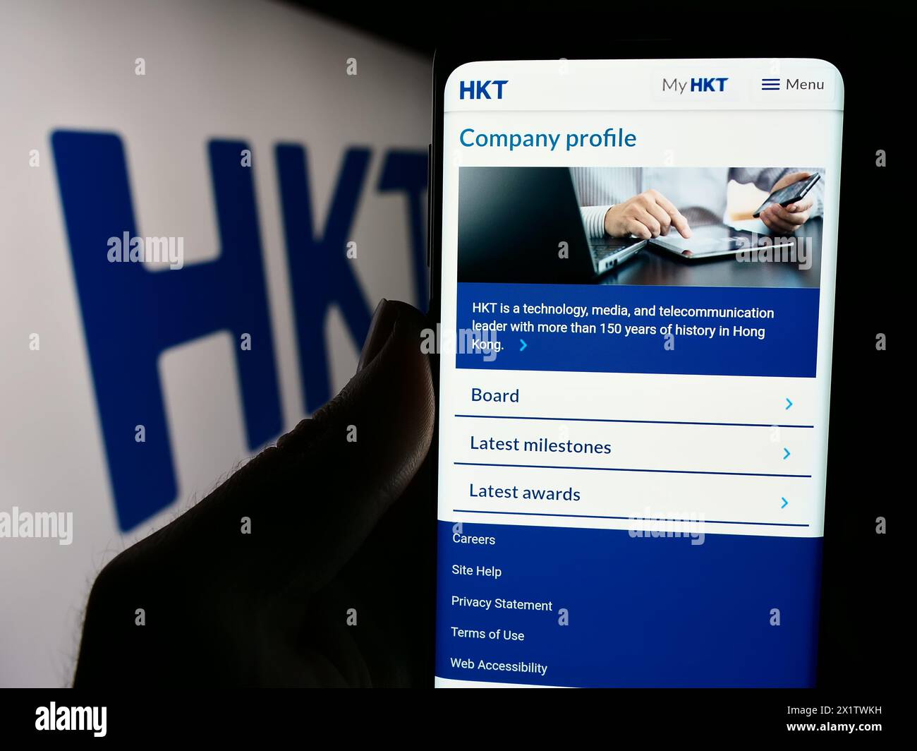 Person mit Smartphone und Webseite des Telekommunikationsunternehmens HKT Limited (Hong Kong Telecom) mit Logo. Konzentrieren Sie sich auf die Mitte des Telefondisplays. Stockfoto