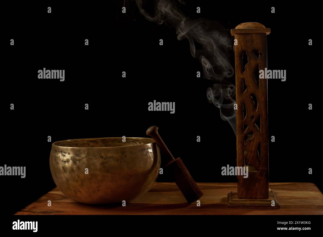 Tibetische Klangschale neben einem hölzernen Räuchergefäß mit Rauch, der auf schwarzem Hintergrund mit Kopierraum herauskommt Stockfoto