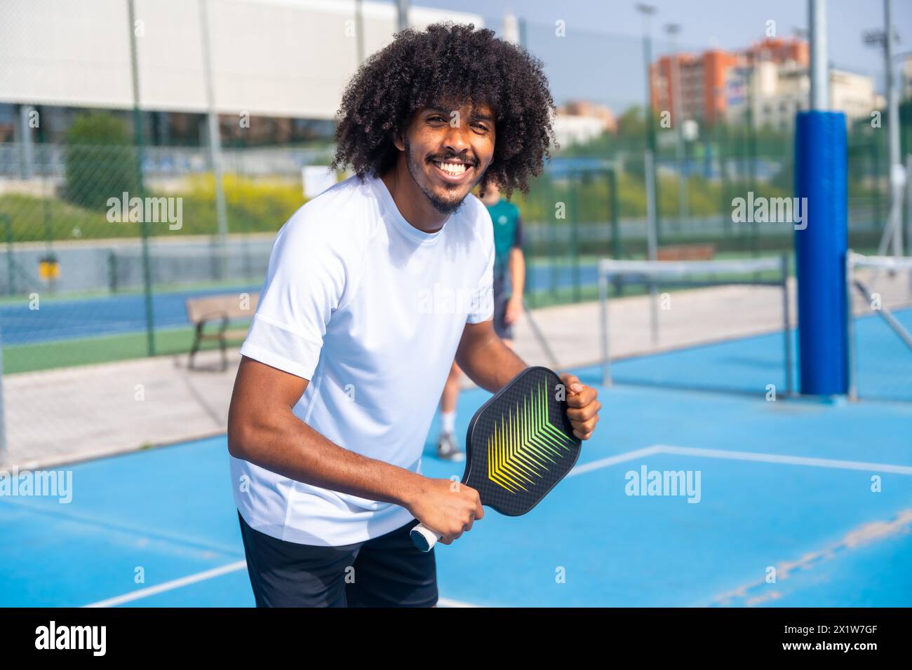 Porträt eines Mannes mit Afro-Frisur, der in die Kamera lächelt und Spaß beim Pickleball im Freien hat Stockfoto