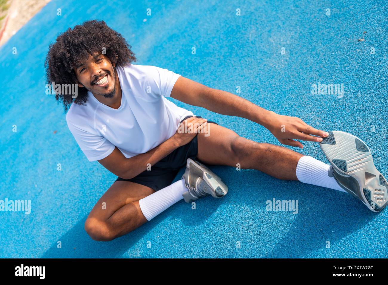 Sportlicher Mann mit Afro-Frisur, der sich auf einer Outdoor-Laufstrecke aufwärmt und dehnt Stockfoto
