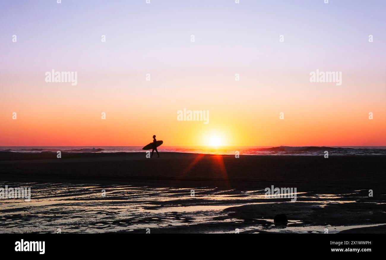 Surfer auf dem Rückweg vom Meer bei Sonnenuntergang Stockfoto