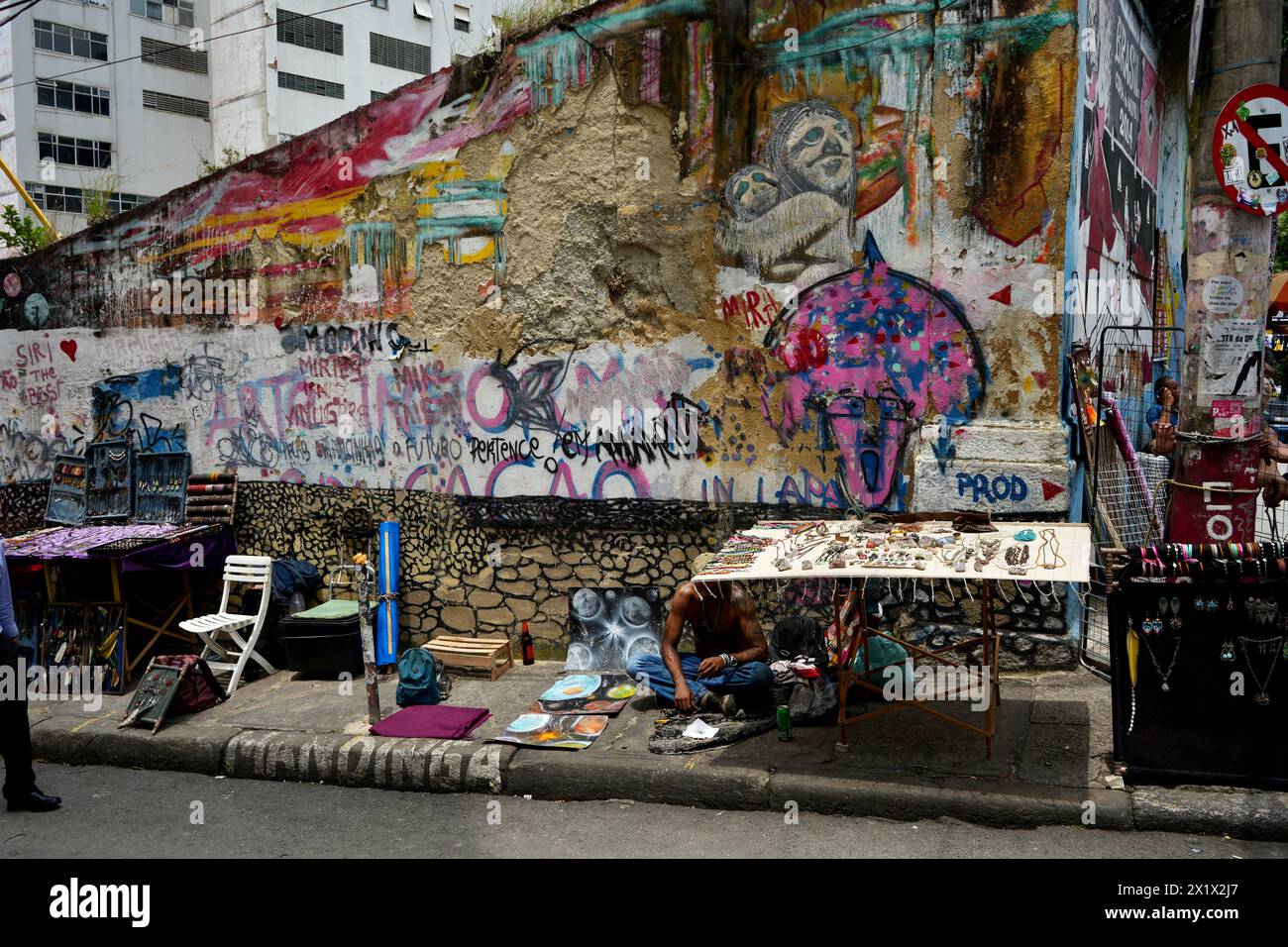 Straßenverkäufer in Lapa in der Nähe der Selaron Steps, mit farbenfroher Straßenkunst dahinter. Stockfoto