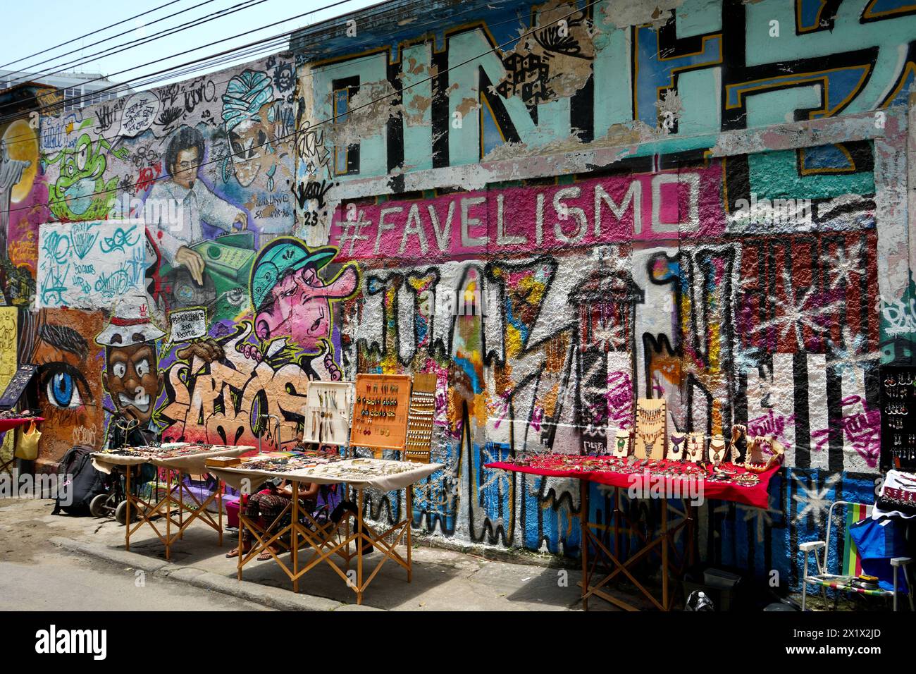 Straßenverkäufer in Lapa in der Nähe der Selaron Steps, mit farbenfroher Straßenkunst dahinter. Stockfoto