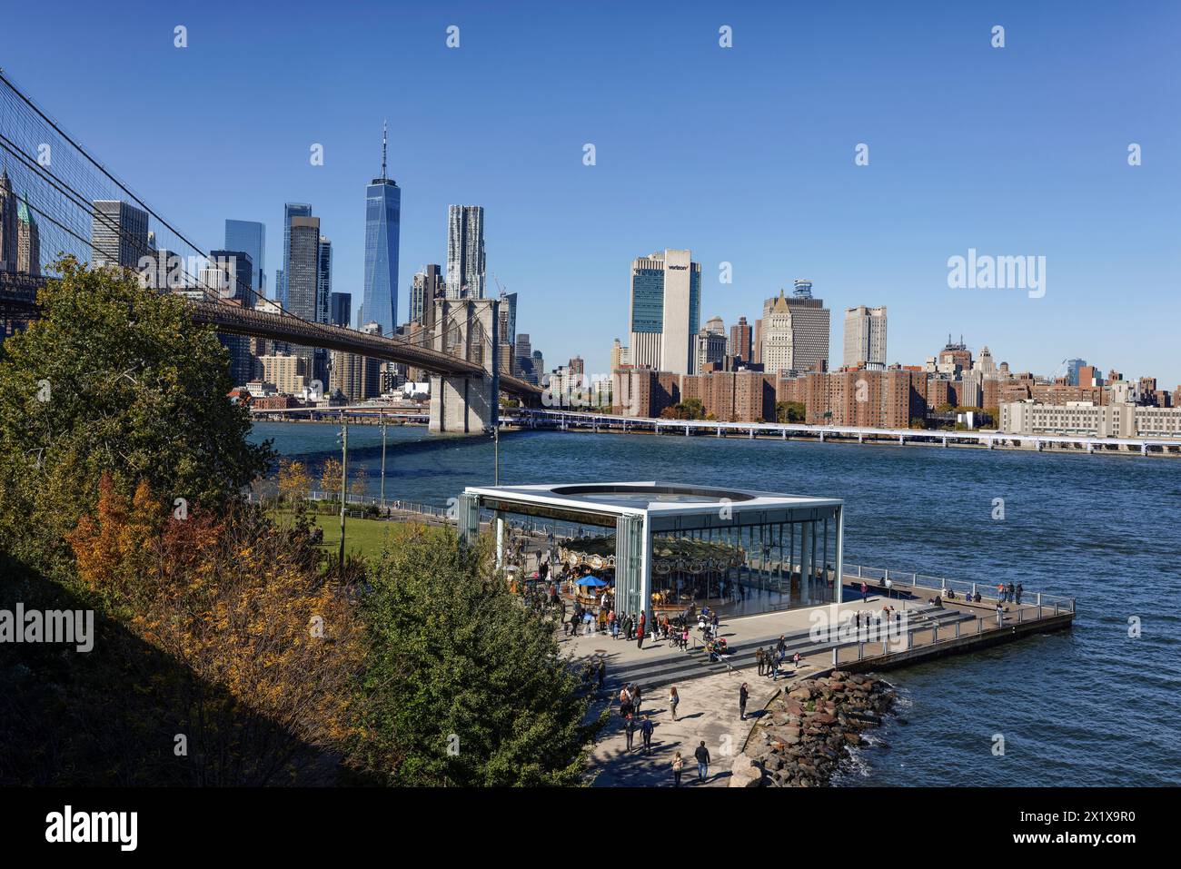 Fahrt mit dem Vergnügungspark Janes Carousel im Brooklyn Bridge Park, Brooklyn mit Brooklyn Bridge, East River und Lower Manhattan Wolkenkratzern dahinter, New York Stockfoto