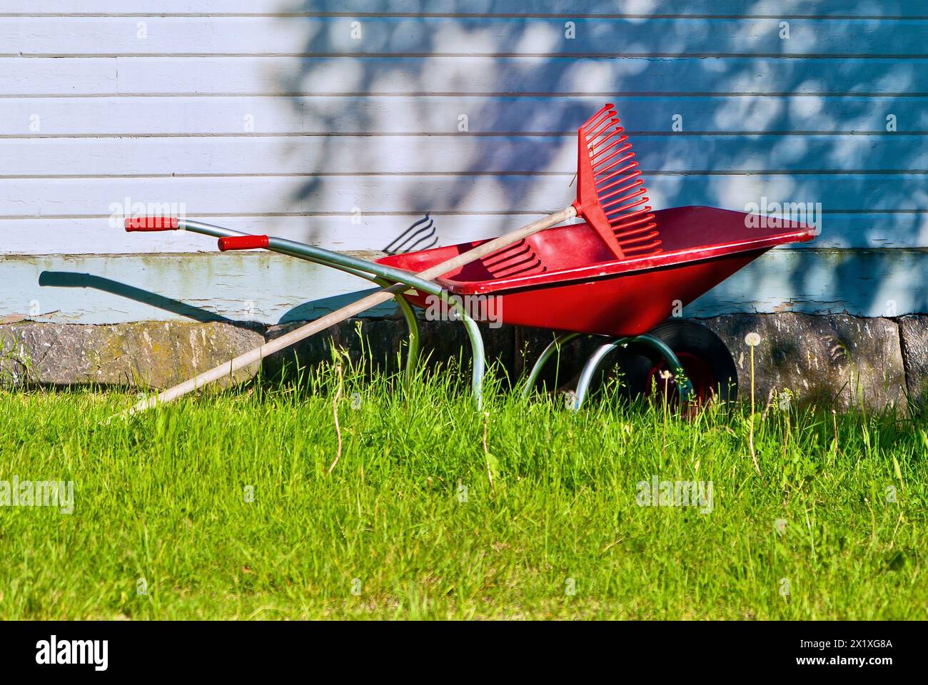 Rote Schubkarre aus Stahl und ein Kunststoffrechen, bereit für den Einsatz im Garten. Stockfoto