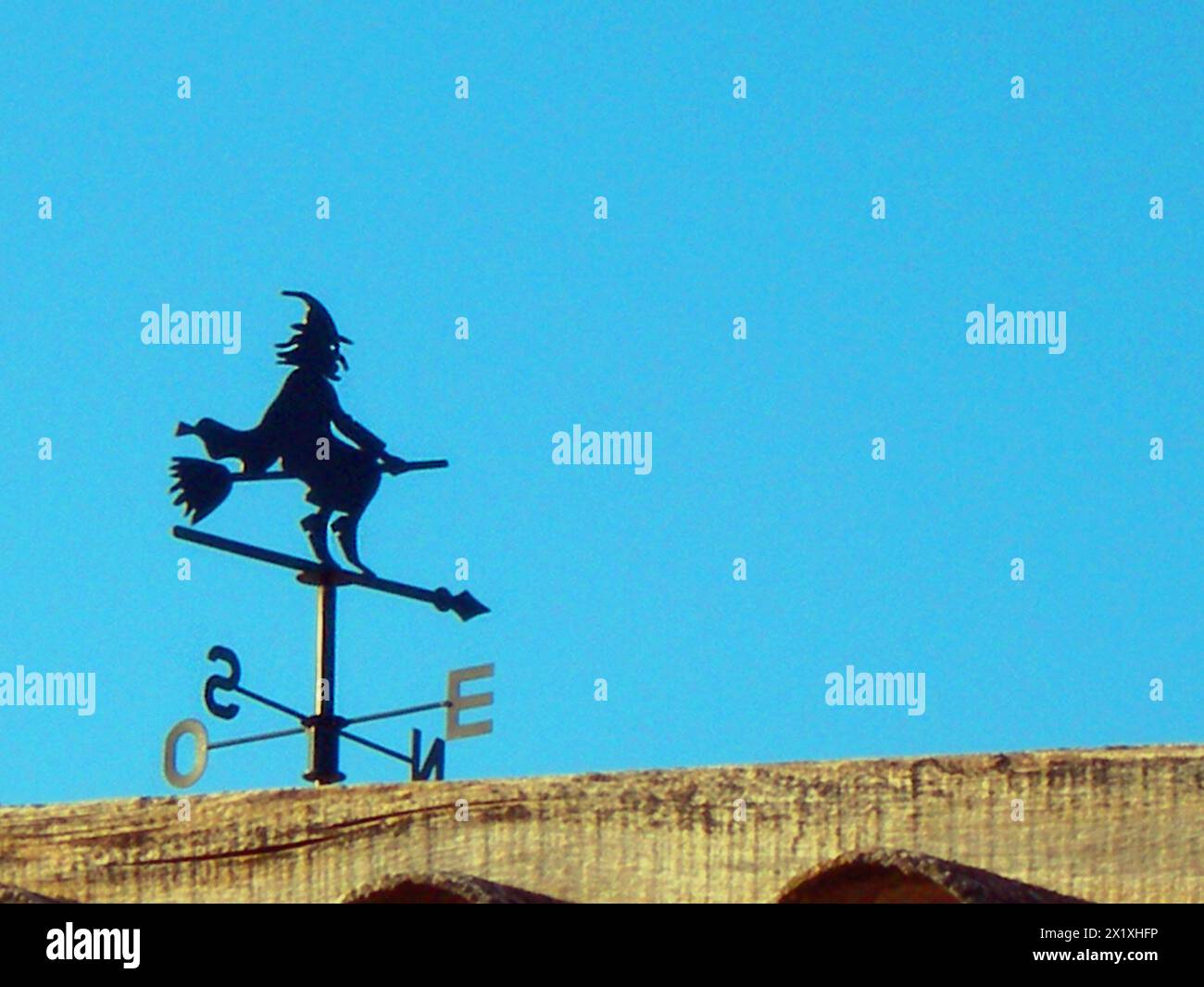 Eine Wetterfahne mit der Figur einer Hexe, die mit einem Besen gegen das Licht reitet, mit Kopierraum. Stockfoto