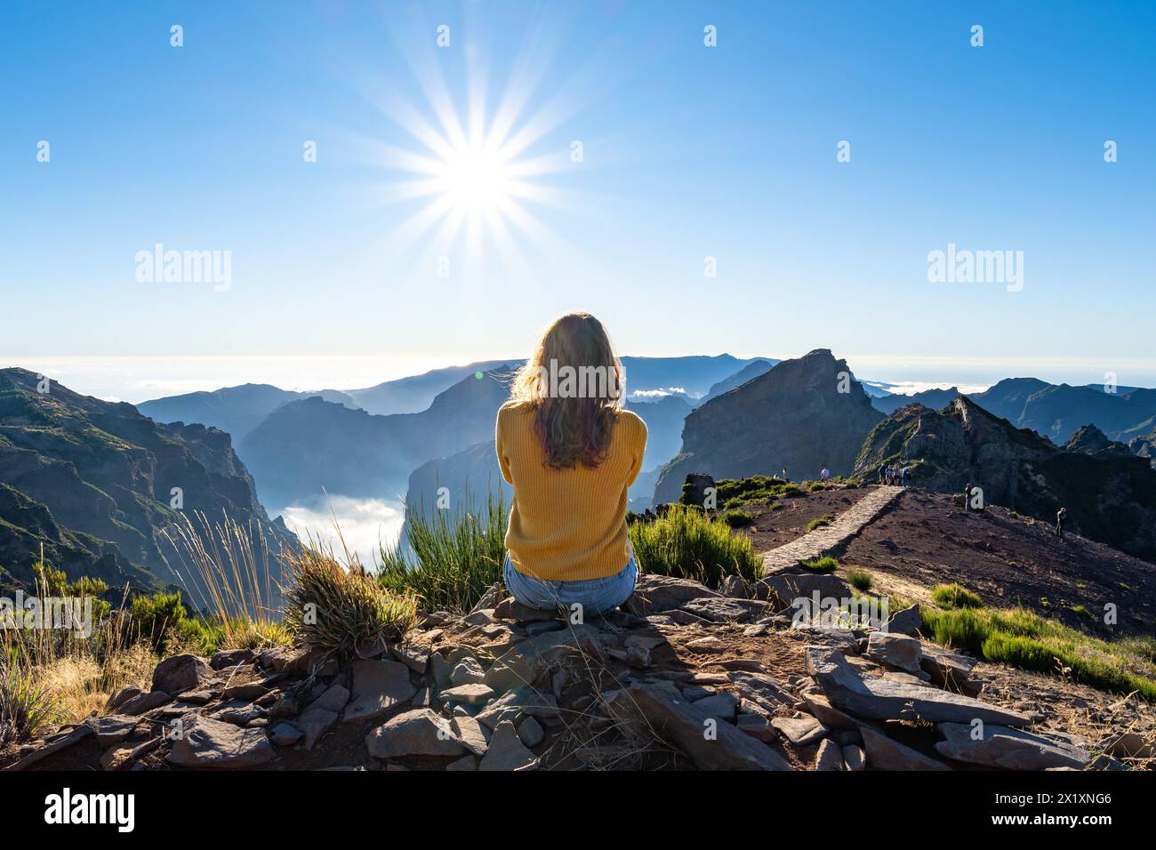 Beschreibung: Eine weibliche Toruistin sitzt auf einem Berg und genießt an einem sonnigen Sommernachmittag den Panoramablick über eine Vulkaninsel. Pico Do Stockfoto