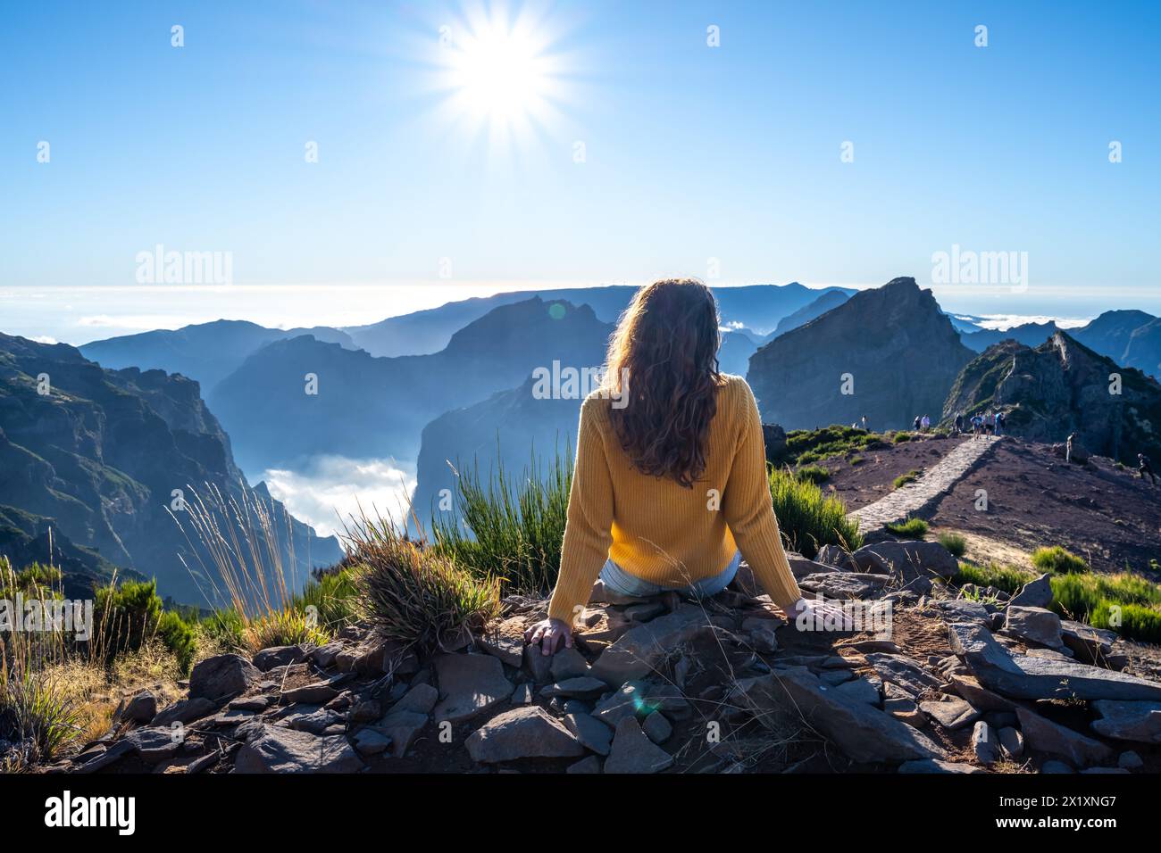 Beschreibung: Weibliche Toruistin sitzt auf dem Gipfel eines Berges und genießt an einem sonnigen Sommernachmittag den Blick auf die Landschaft einer Vulkaninsel. Pi Stockfoto