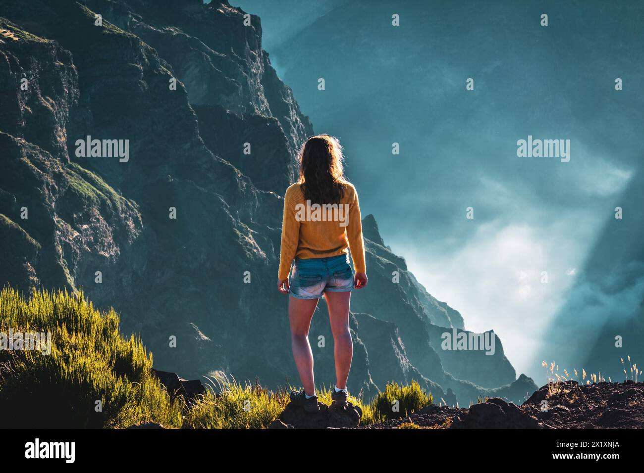 Beschreibung: Sportlicher Frauentoursit überblickt die atemberaubenden Tiefen eines wolkenbedeckten Tals und genießt den Blick auf die vulkanische Berglandschaft. Stockfoto