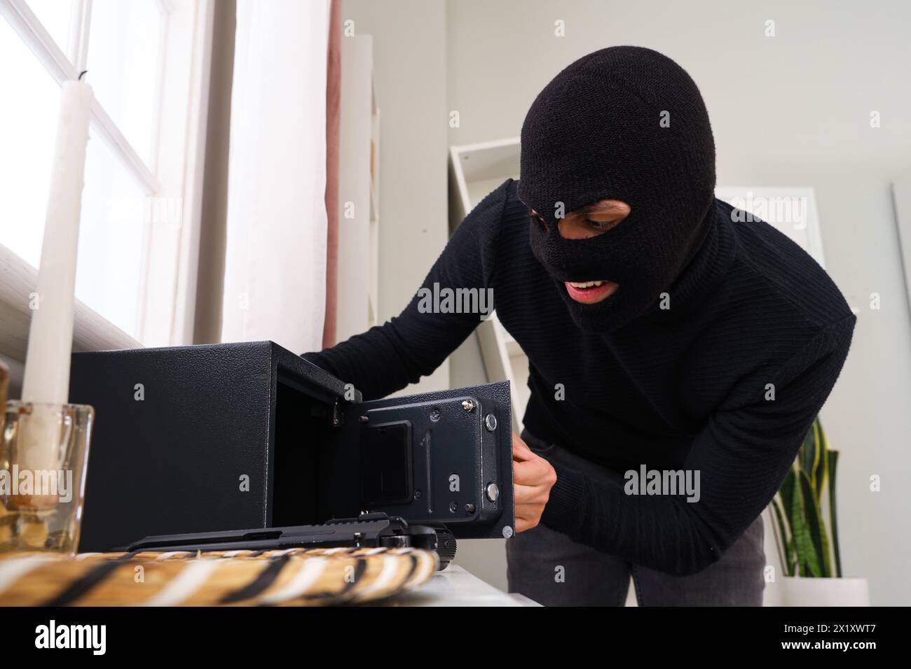 Männlicher Dieb bricht in den Safe im Zimmer ein Stockfoto