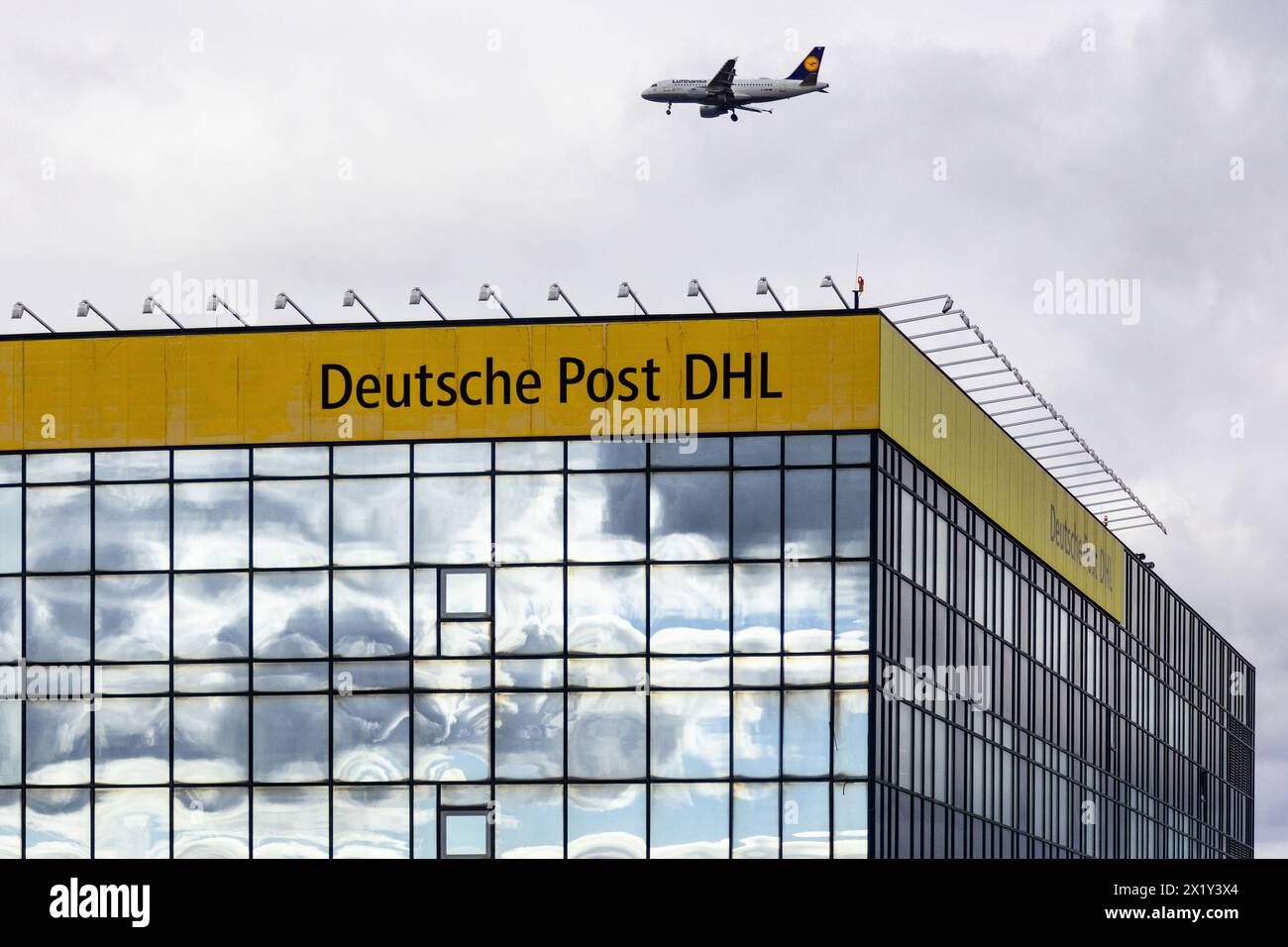 Frankfurt International Airport, Deutschland - 19. Februar 2024: Ein Flugzeug fliegt über einem Gebäude mit der Marke 'Deutsche Post DHL' und einem reflektierenden f Stockfoto