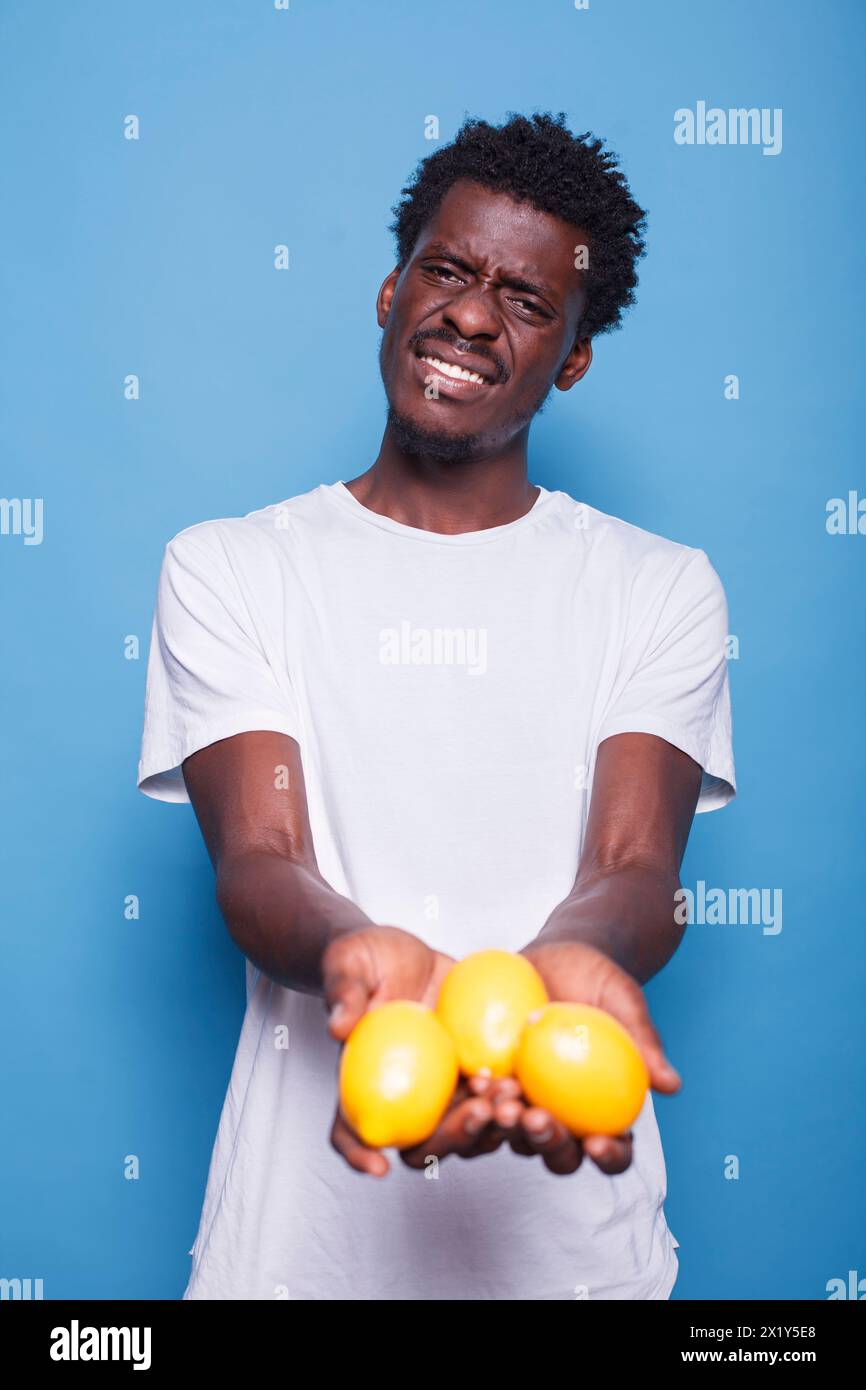 afroamerikaner, der Zitronen für eine gesunde vegetarische Ernährung hält. Mann, der gelbe Zitrusfrüchte in den Händen zur natürlichen Ernährung mit Vitaminen präsentiert. Erwachsener zeigt frische saftige Früchte vor der Kamera. Stockfoto
