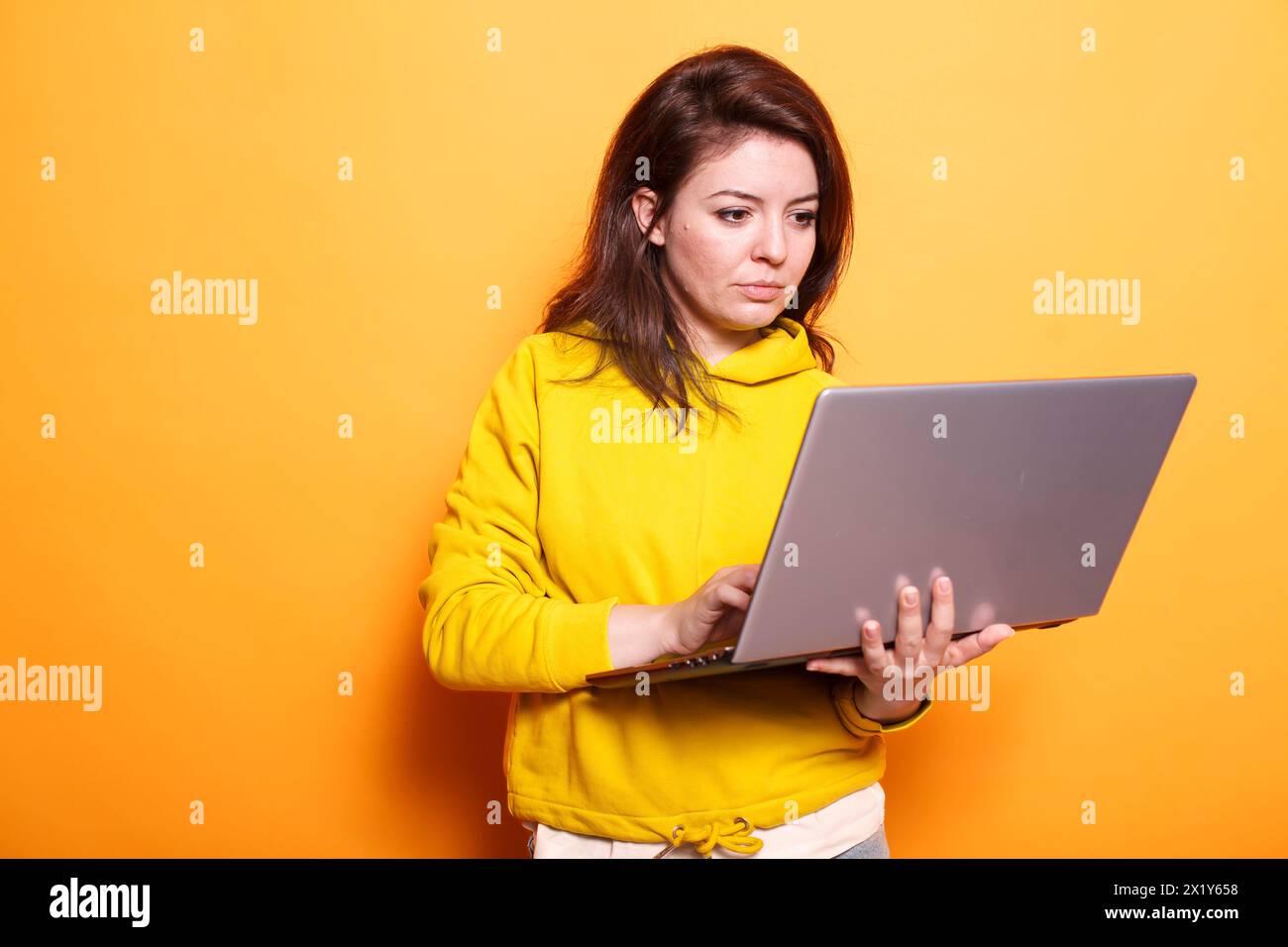 Freiberuflich tätige Frau, die moderne Technologie nutzt, indem sie digitale Laptops nutzt. Porträt einer fokussierten Frau, die online auf einem drahtlosen Computer arbeitet, während sie über einem isolierten orangefarbenen Hintergrund steht. Stockfoto