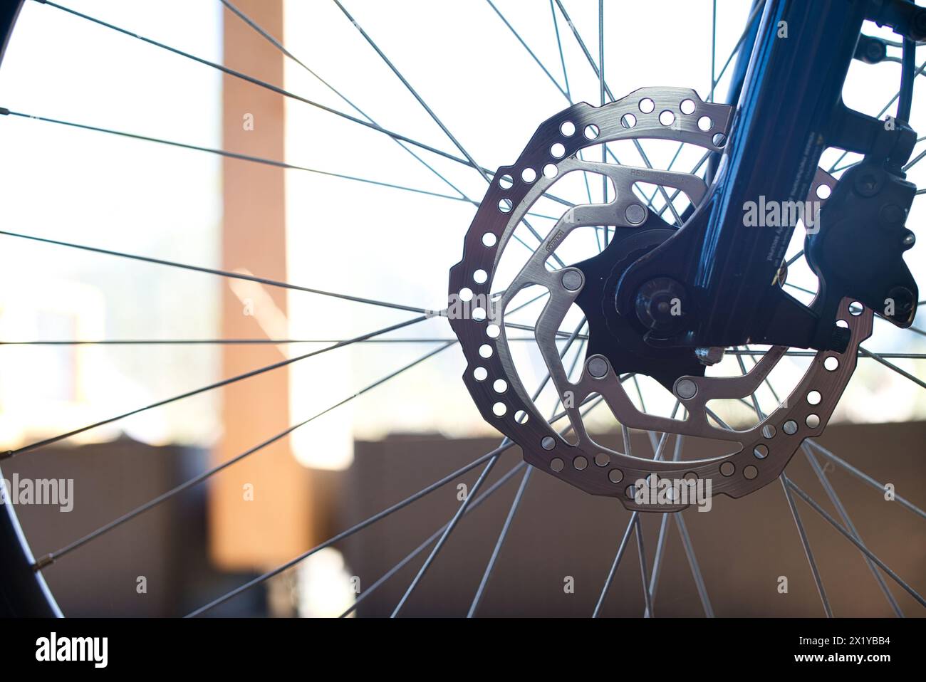 Nahaufnahme des Vorderrads eines E-Bikes mit einer Bremsscheibe aus Edelstahl, einem Bremssattel und einem Abschnitt der dunkelblauen Hochglanzgabel. Stockfoto
